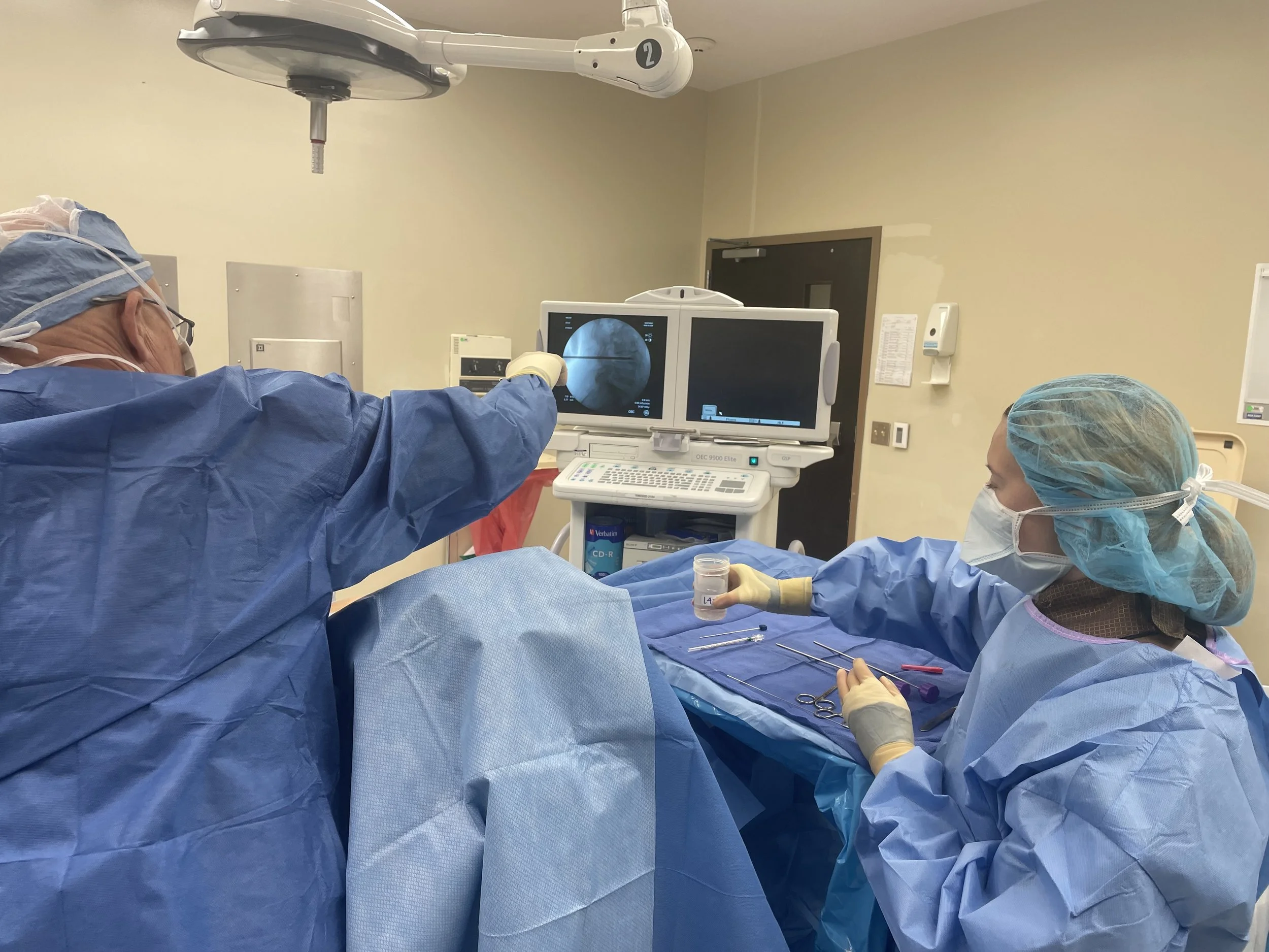 Medical professionals in surgical attire performing a procedure in an operating room with monitors and medical equipment.