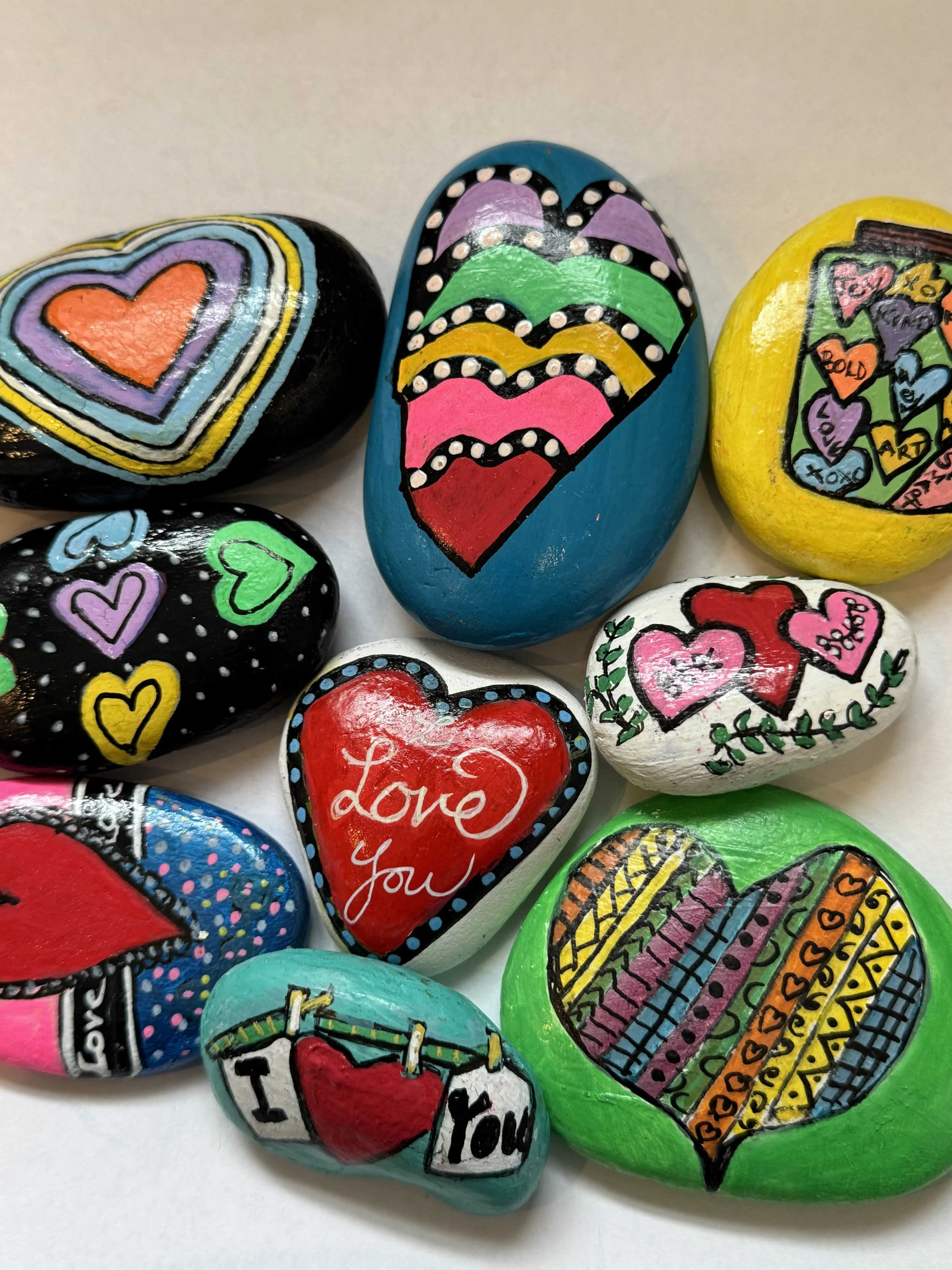 Colorful painted rocks with heart and love designs, including phrases like "Love you" and decorative patterns.