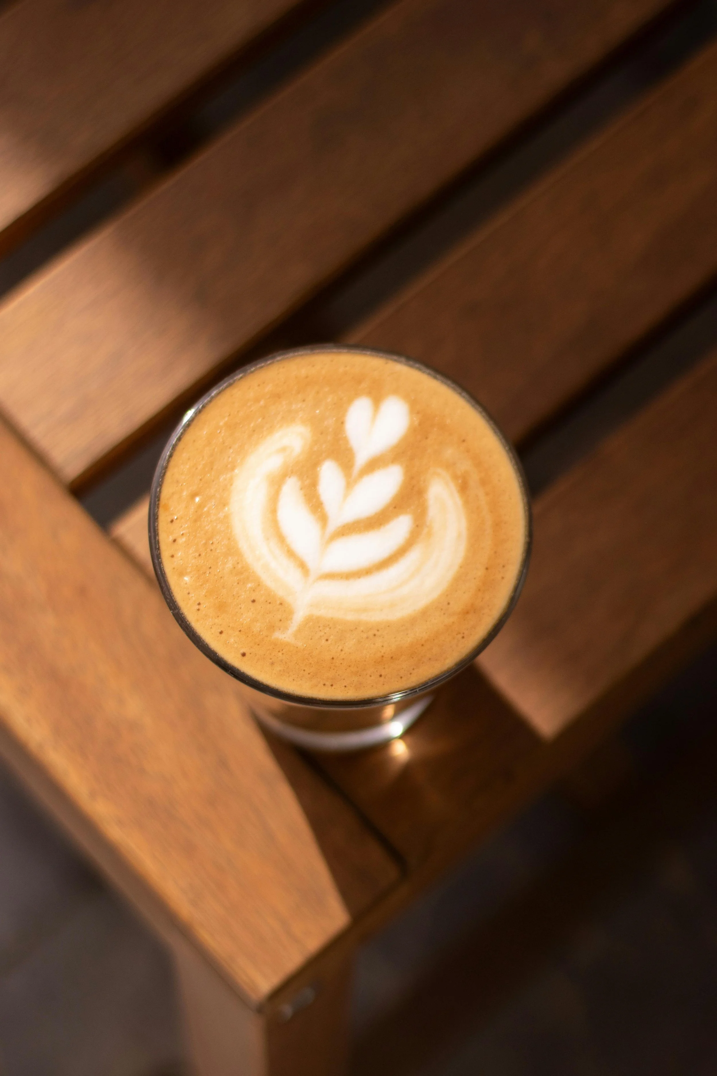 Un verre de cappuccino avec un motif en forme de feuille de latte art, placé sur une table en bois
