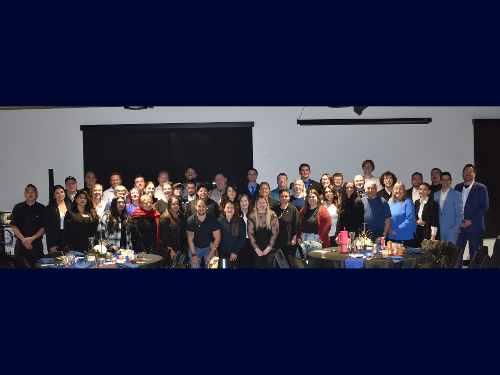 A large group of people gathered in a banquet hall for a group photo, with tables and decorations visible in the foreground.