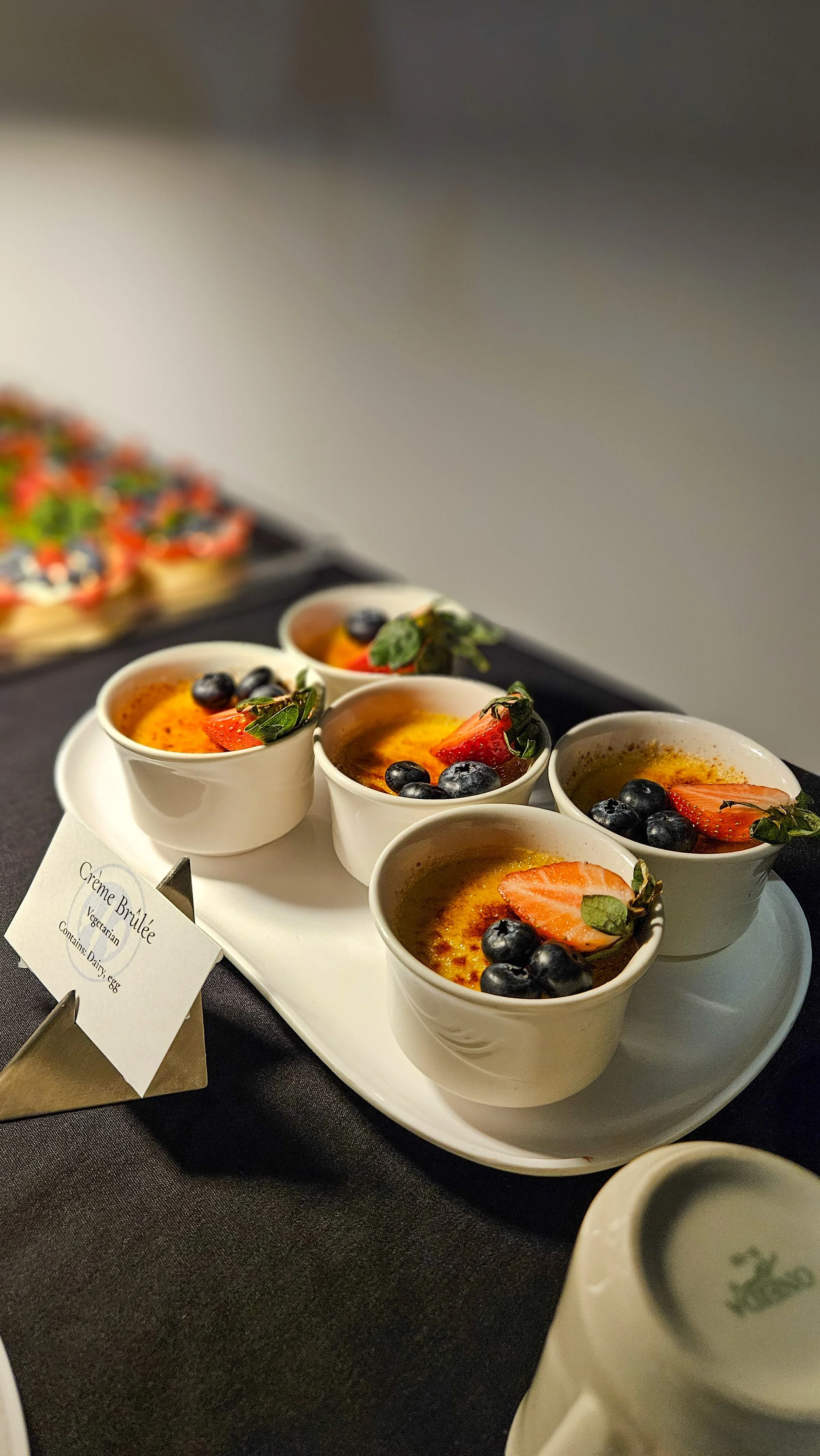 Four small white ramekins filled with creme brulee topped with fresh strawberries and blueberries, placed on a white serving tray.