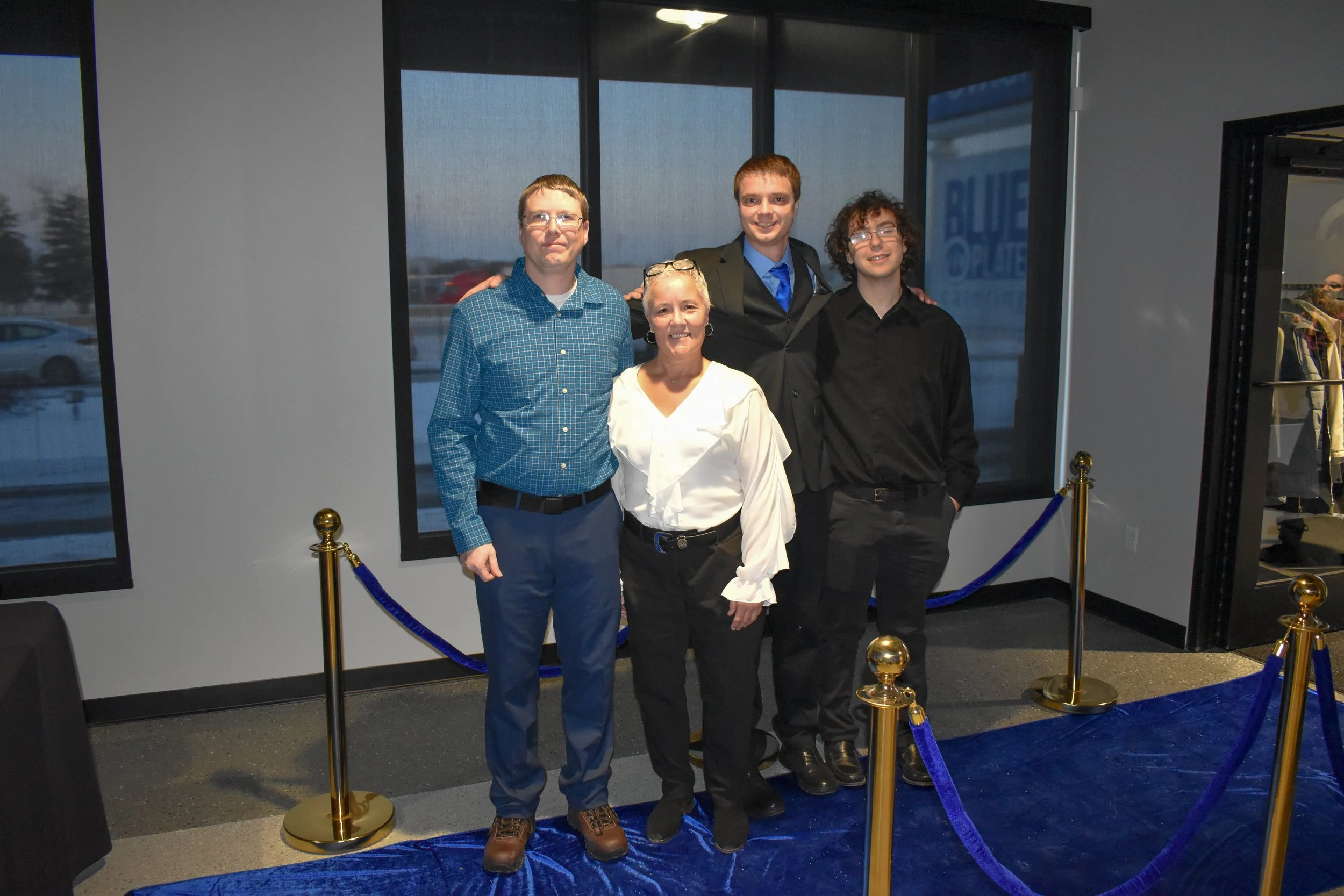 A group of five people, three young men and two women, standing together inside a building near large windows with a snowy outdoor scene visible, posing for a photo.