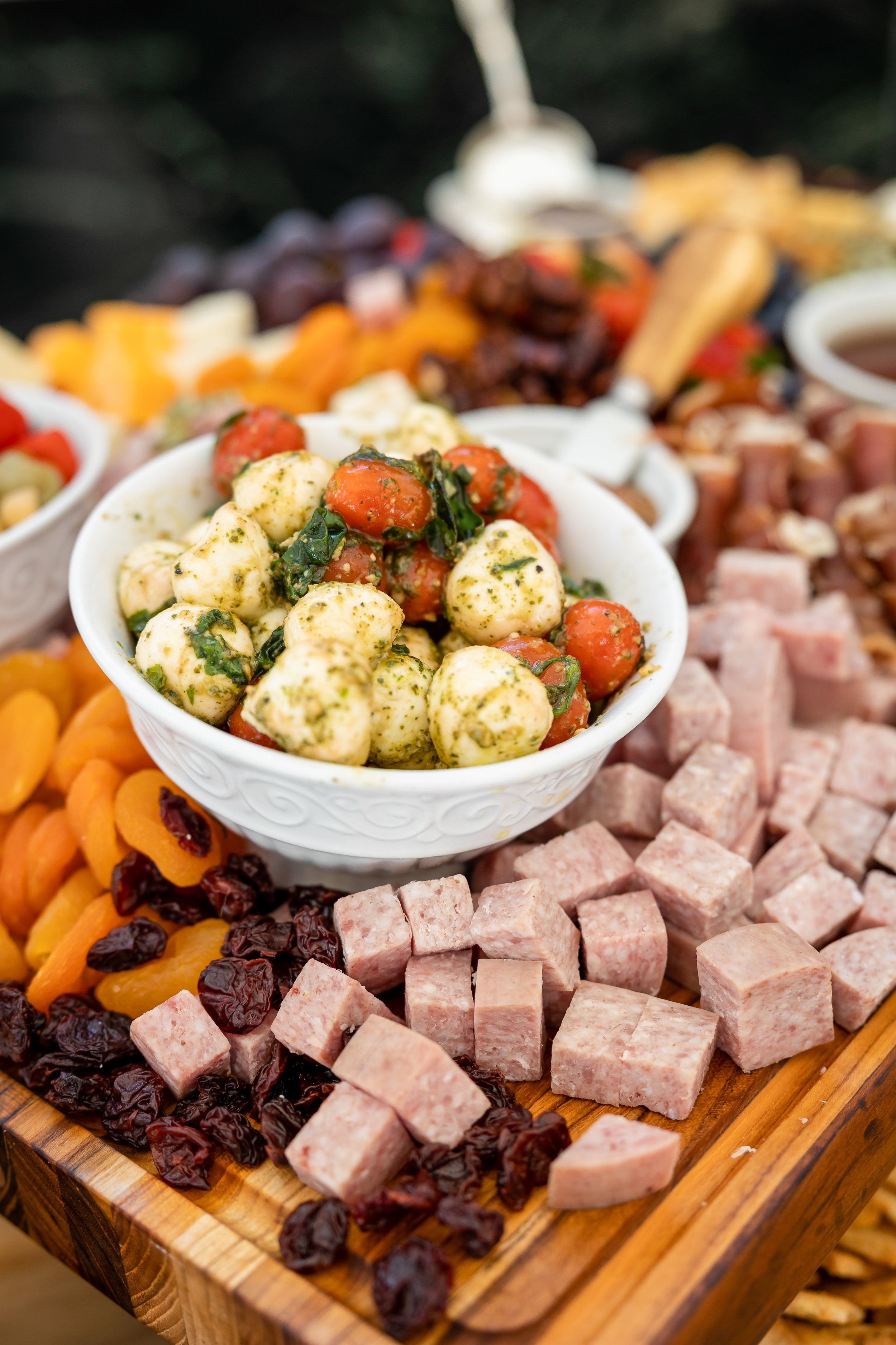 A platter of assorted cold cuts, cheeses, dried fruits, and a bowl of marinated cheese balls.
