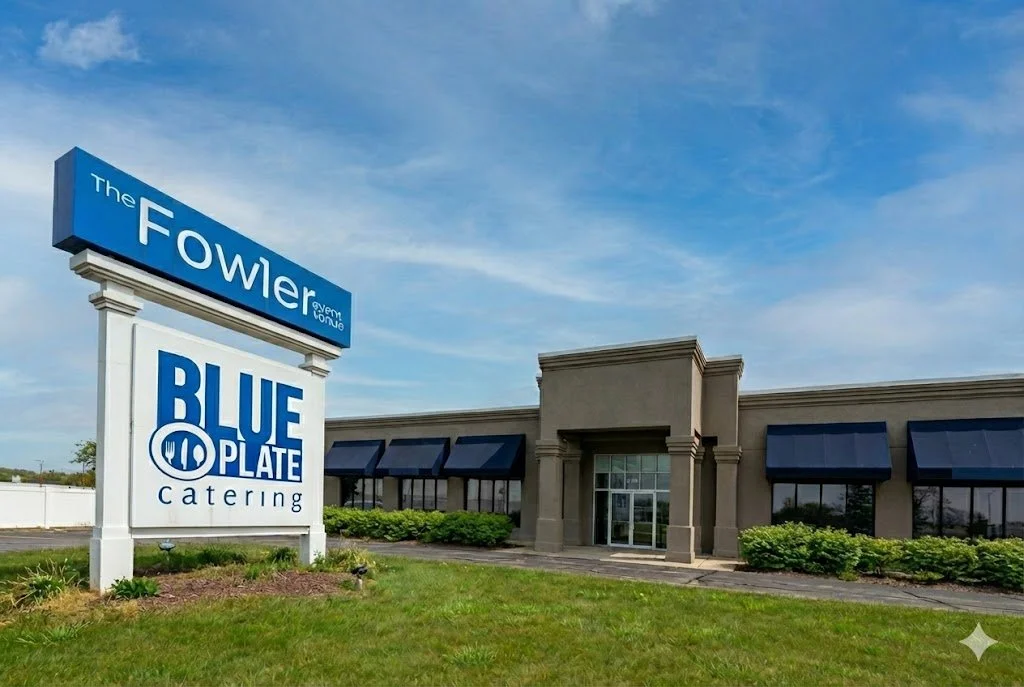 Exterior of a catering restaurant named 'Blue Plate Catering' with a large sign and a strip mall building in the background under a blue sky.