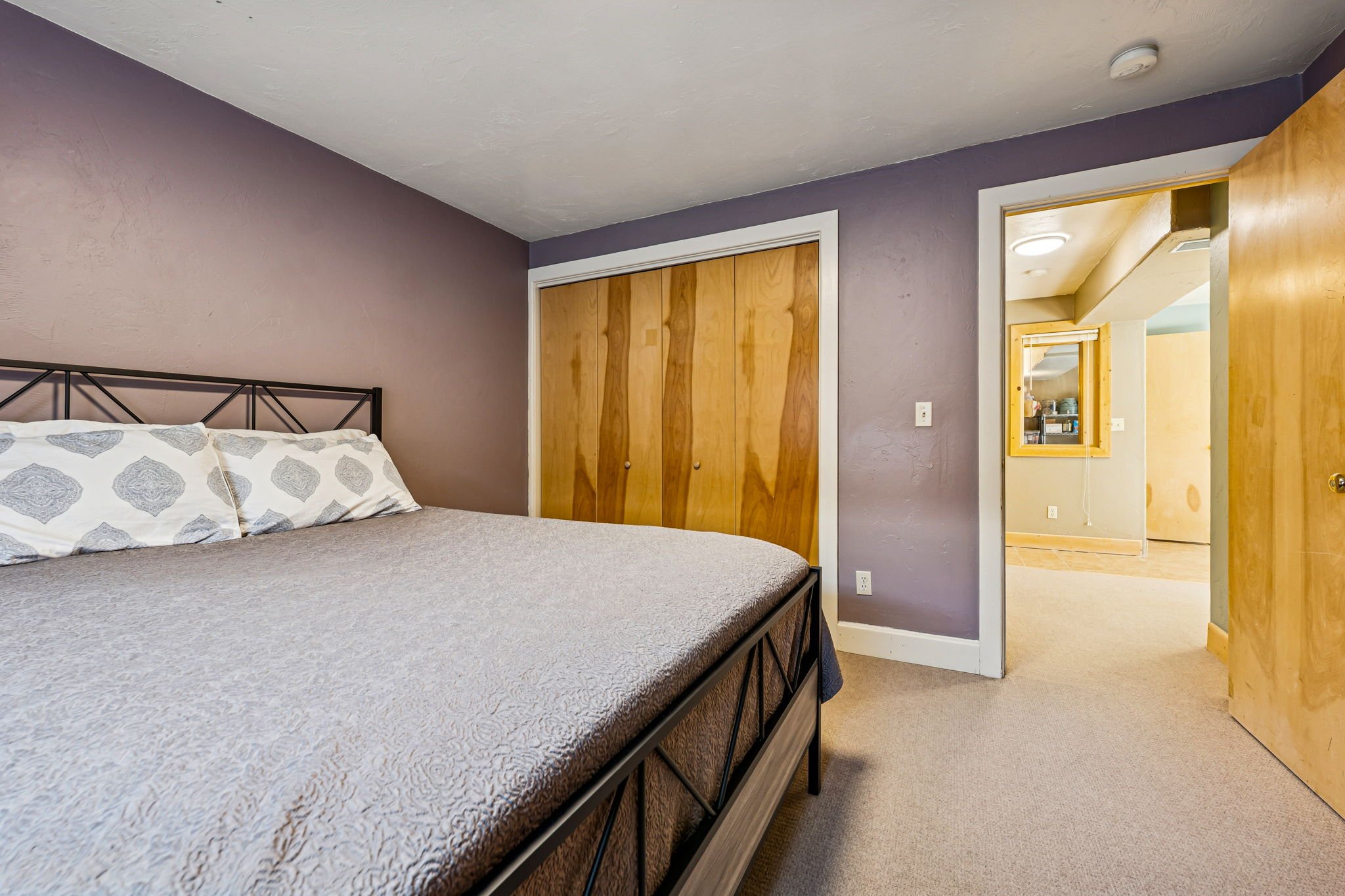 Bedroom with a bed, purple wall, wooden closet doors, and an open doorway leading to a hallway.