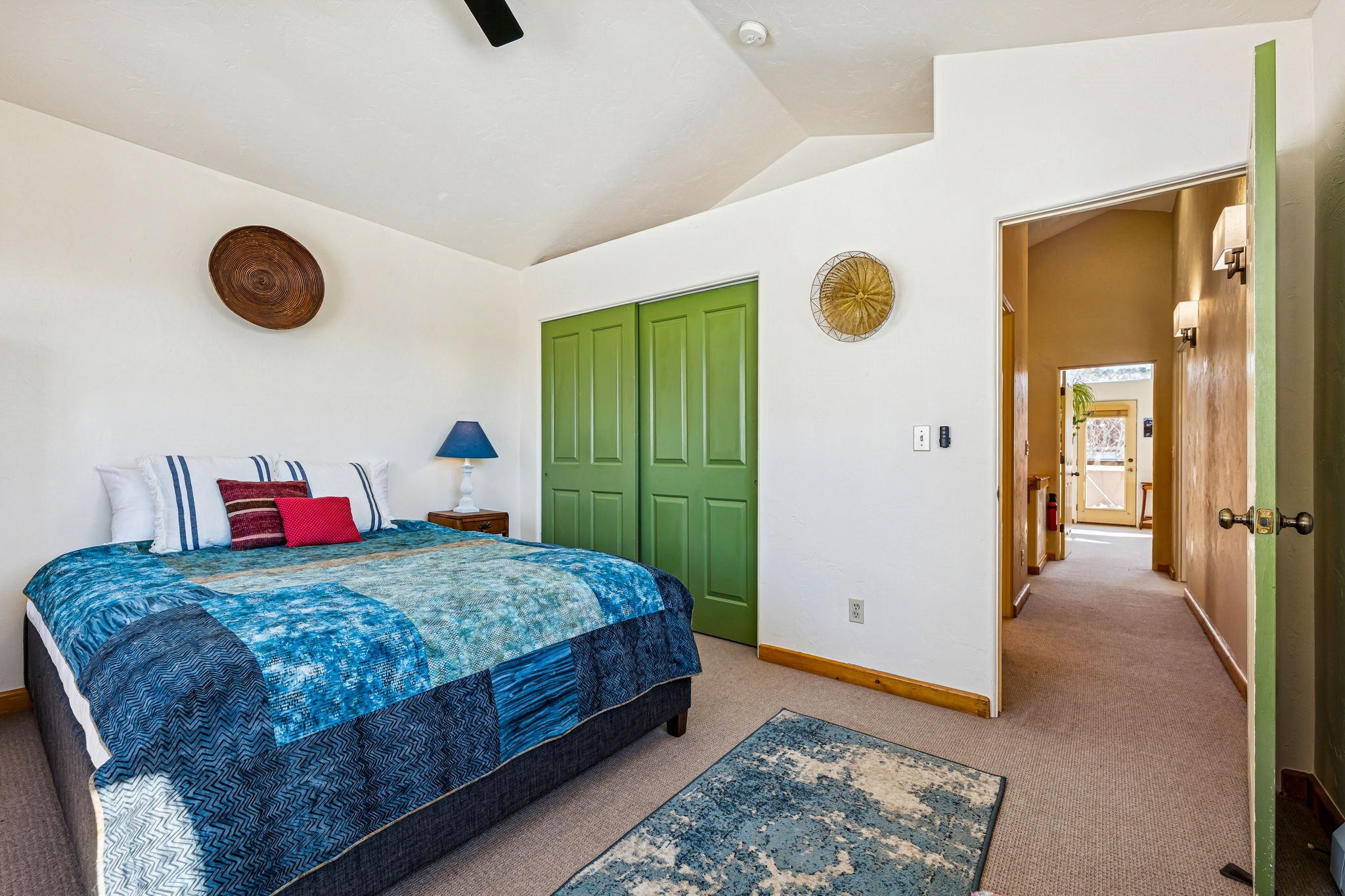 A bedroom with a blue quilted bed, green closet doors, a nightstand with a blue lamp, and decorative wall baskets.
