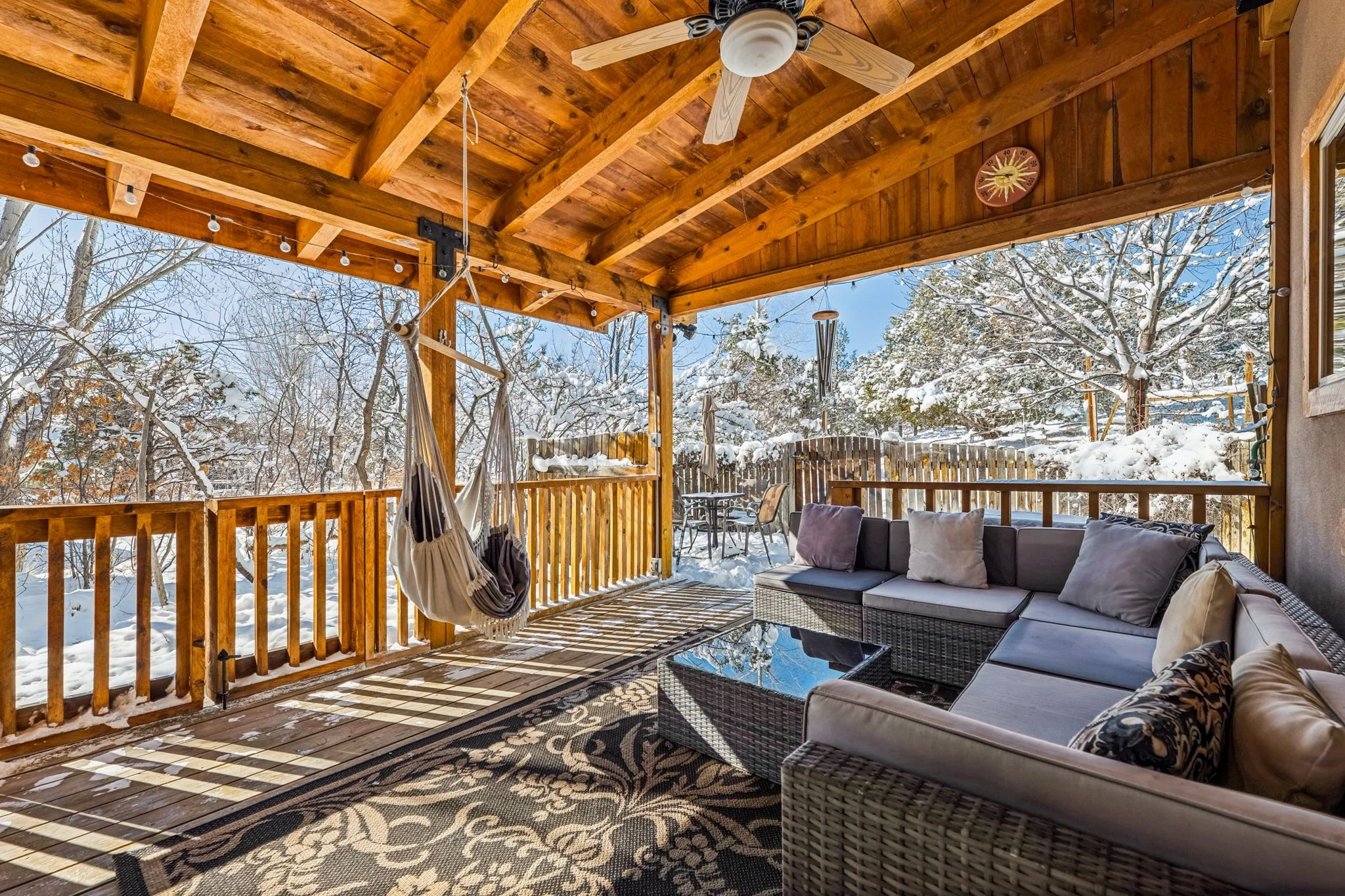  covered porch with outdoor seating and swing, overlooking a snowy yard with trees and snow-covered outdoor furniture, wood ceiling and railing