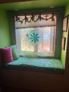 A cozy window seat with colorful pillows and a green floral cushion, decorated with garland, in front of a large window with a floral decal on the glass.