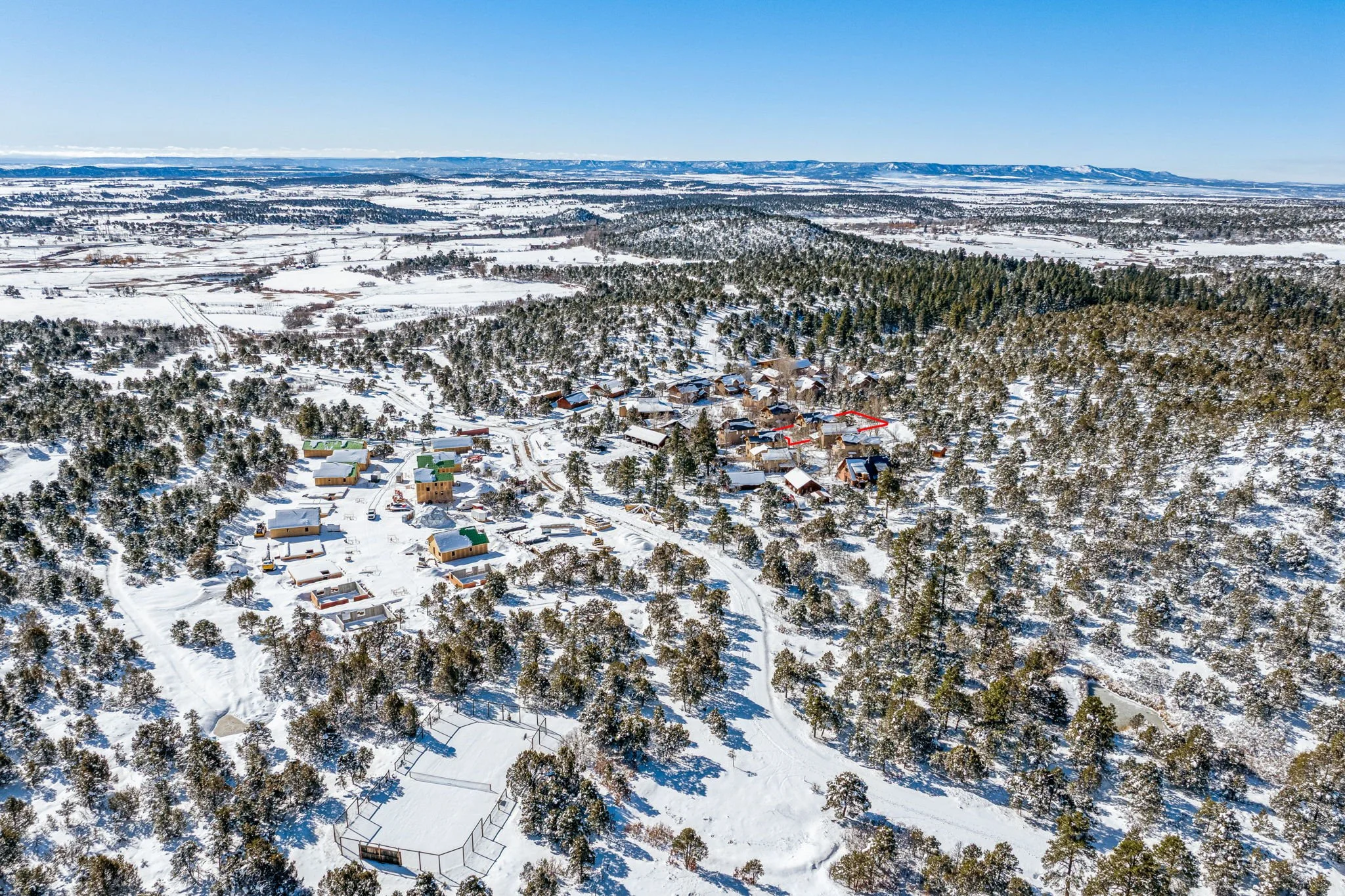 A snowy landscape with a cluster of houses and trees, viewed from above, in a rural area under a clear blue sky.