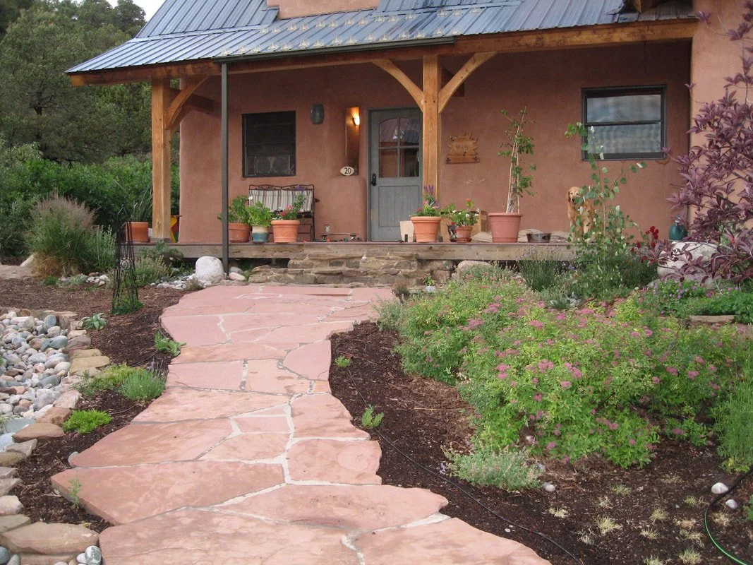 A house with a porch, potted plants, a dog, and a stone pathway leading to the porch.