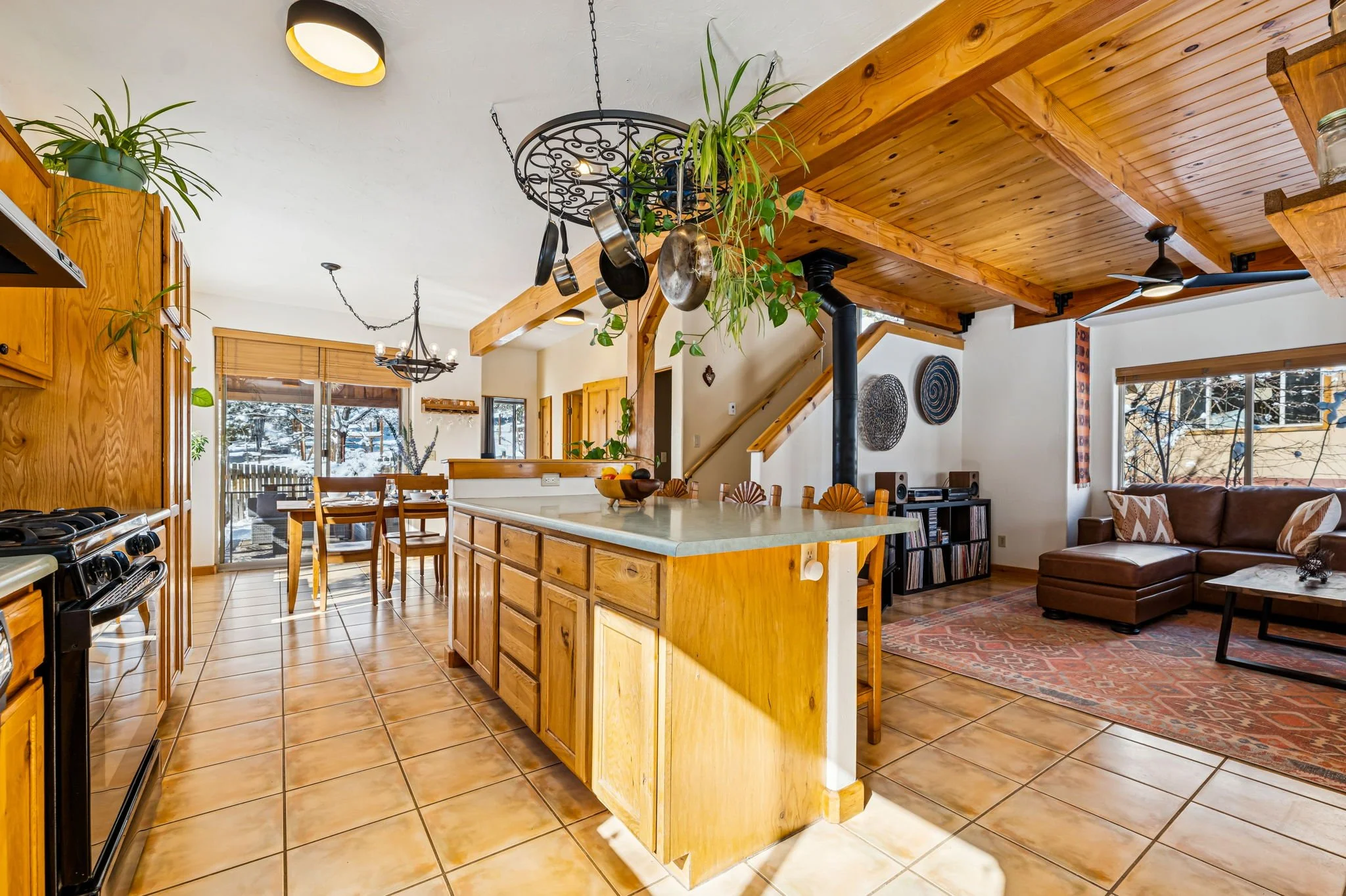Open-concept kitchen and living room with wooden cabinets, tile flooring, and large windows showing snowy outdoor scenery