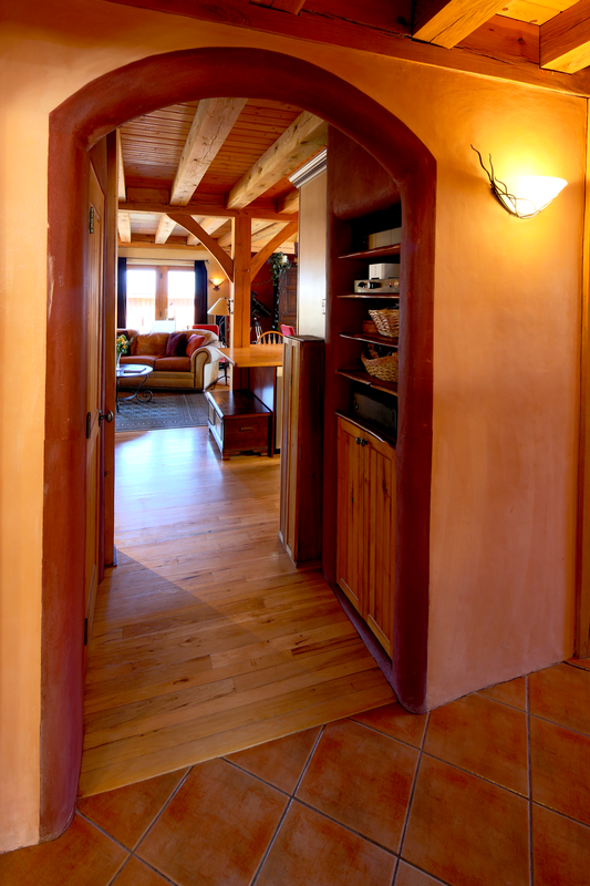 View through an arched doorway into a living room with wooden beams, a sofa, and windows