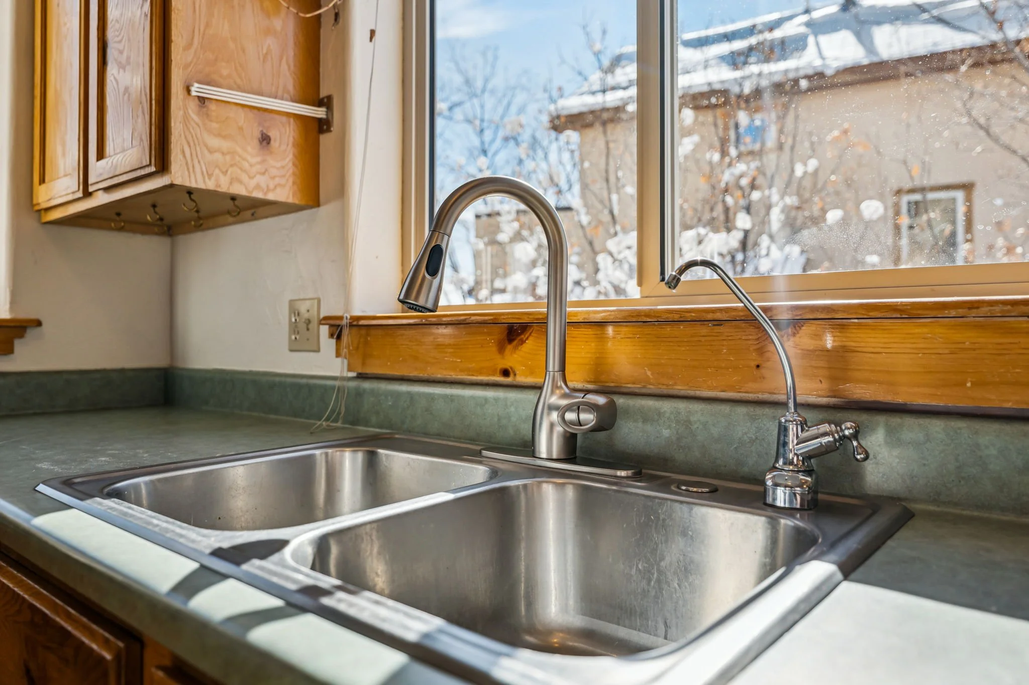 Kitchen sink with double stainless steel basins, faucet, and window showing snowy outdoor scene.