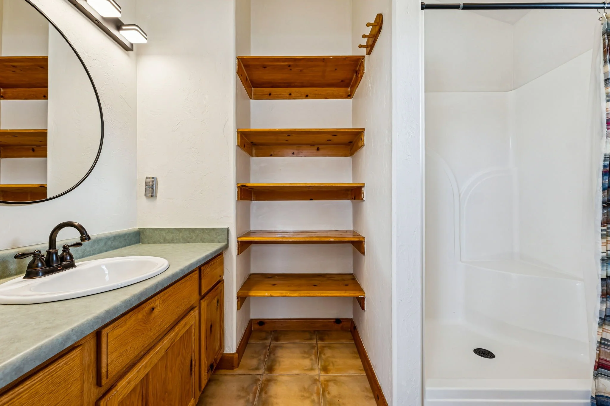 Bathroom with wooden shelves, a sink with a cabinet, a mirror, and a shower with a curtain.