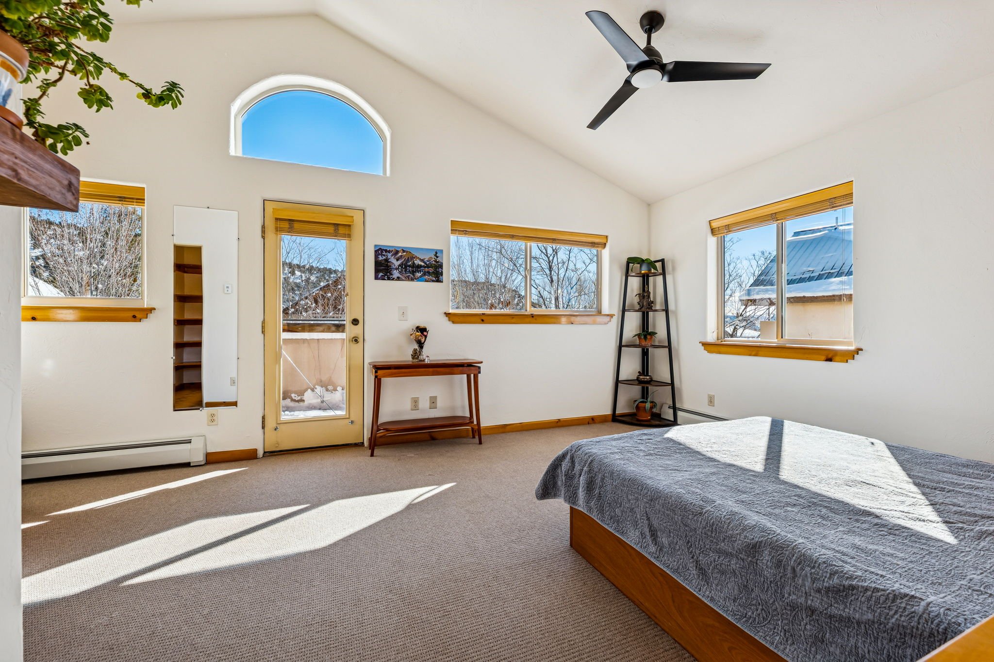 Empty bedroom with a bed, multiple windows, a ceiling fan, and a door leading to a balcony with snow outside.