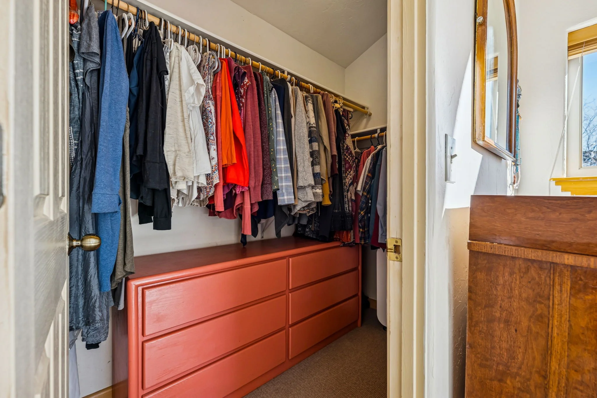 A walk-in closet with hanging clothes and a large dresser beneath the hanging clothes.