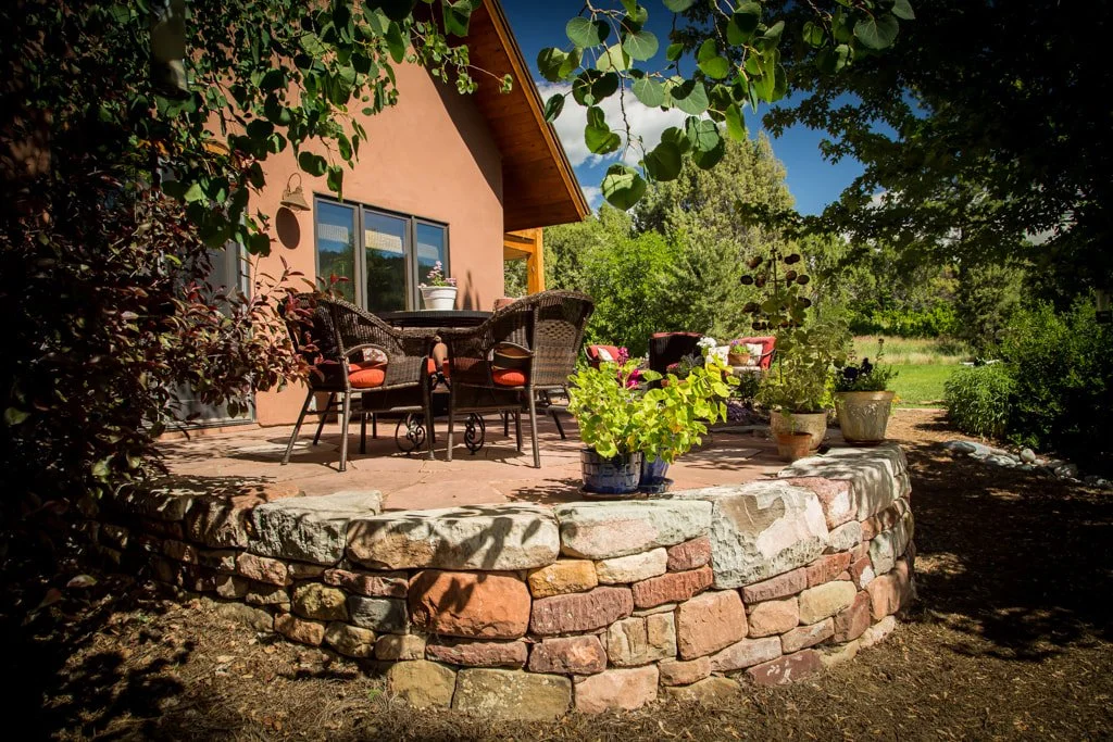 A backyard patio with outdoor furniture, potted plants, and trees surrounding the area.