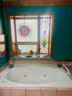 A bathroom with a jacuzzi tub beneath a window, decorated with plants and stained glass art, with teal walls.