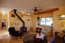 Living room with a white sofa, black armchair, wooden coffee table, and a fireplace with a wood-burning stove, large window with curtains, yellow walls, and ceiling fan.