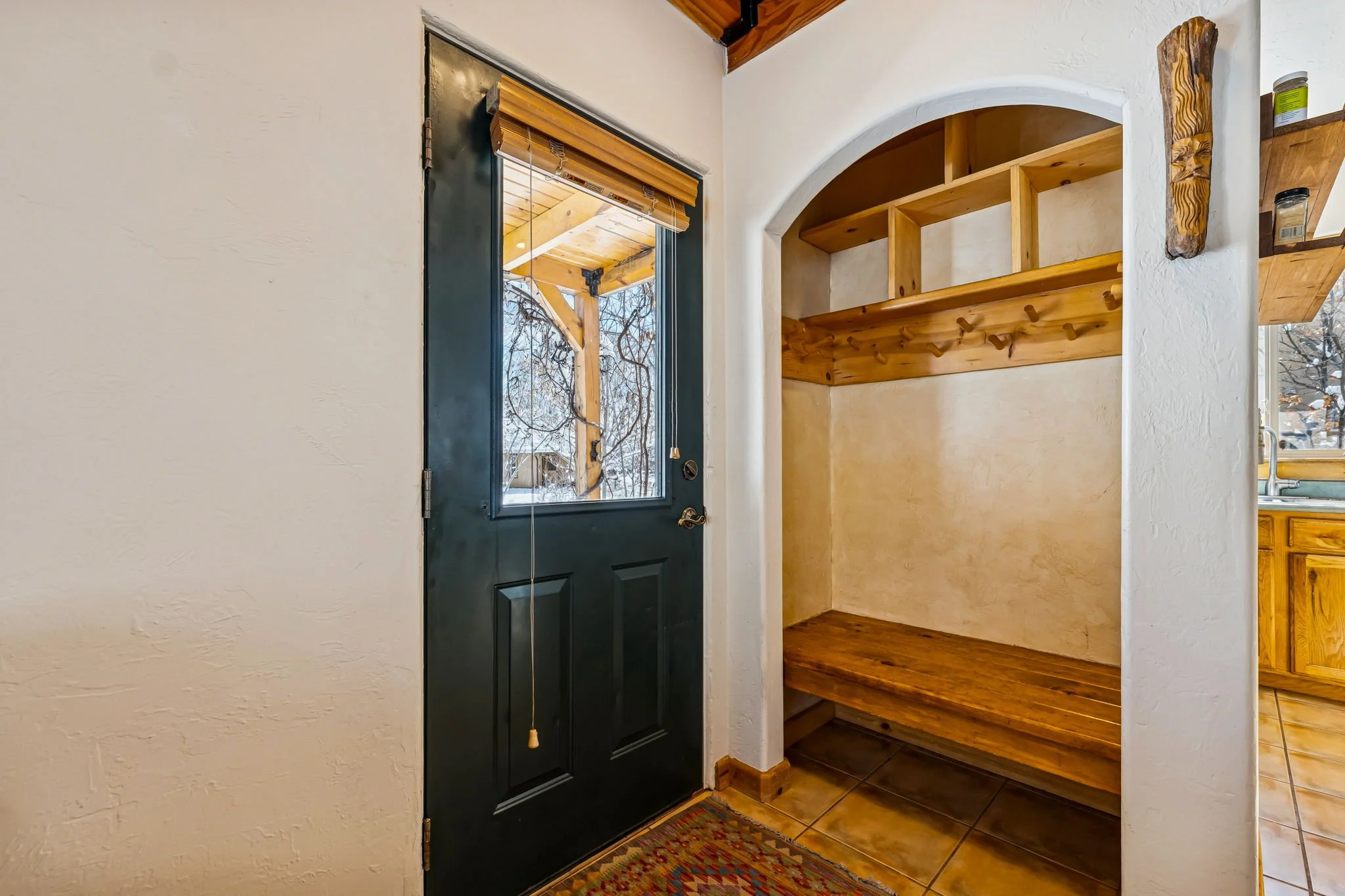 View of a front door with a small window and a wooden coat rack with hooks and shelves in an entryway with tiled floor.