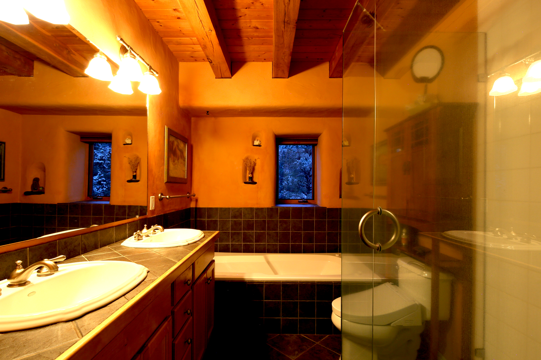 Bathroom with double sink vanity, bathtub, toilet, wood accents, and small windows showing a snowy landscape outside.