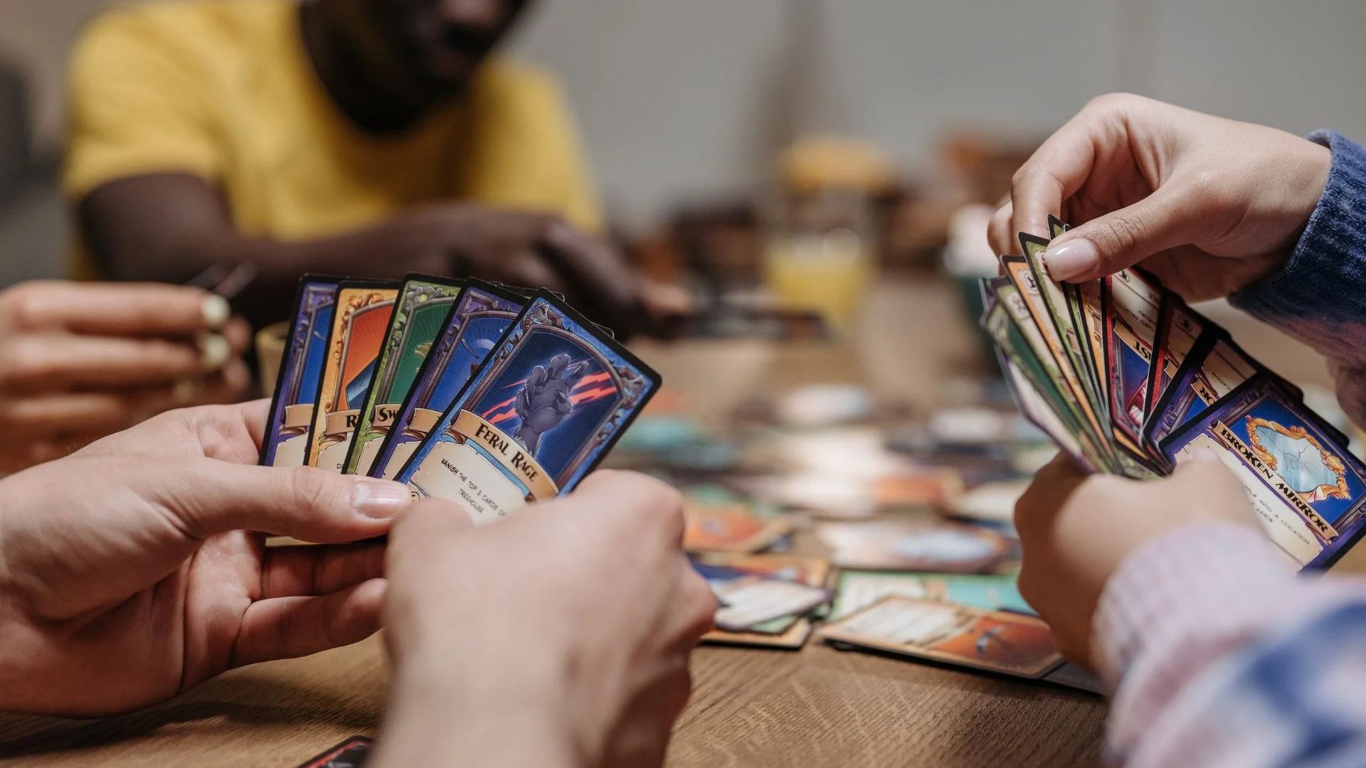 Four people sit at a table playing a tabletop game with cards in their hands