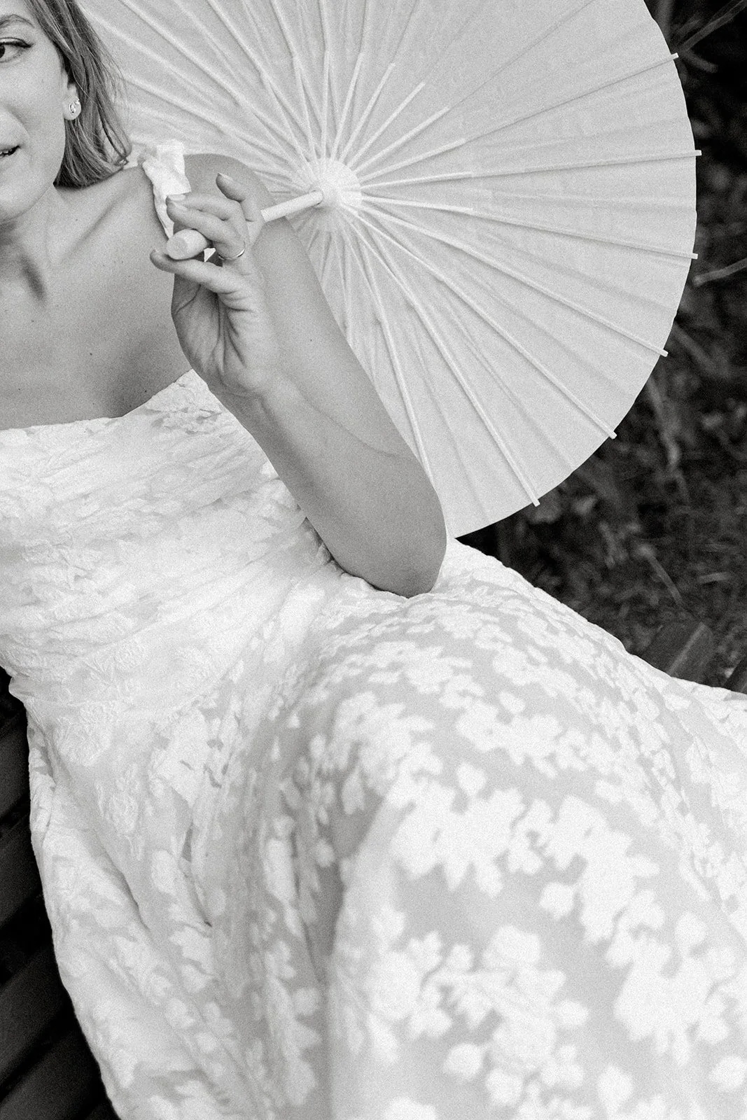 A woman in a lace dress holding a paper parasol, sitting on a bench.
