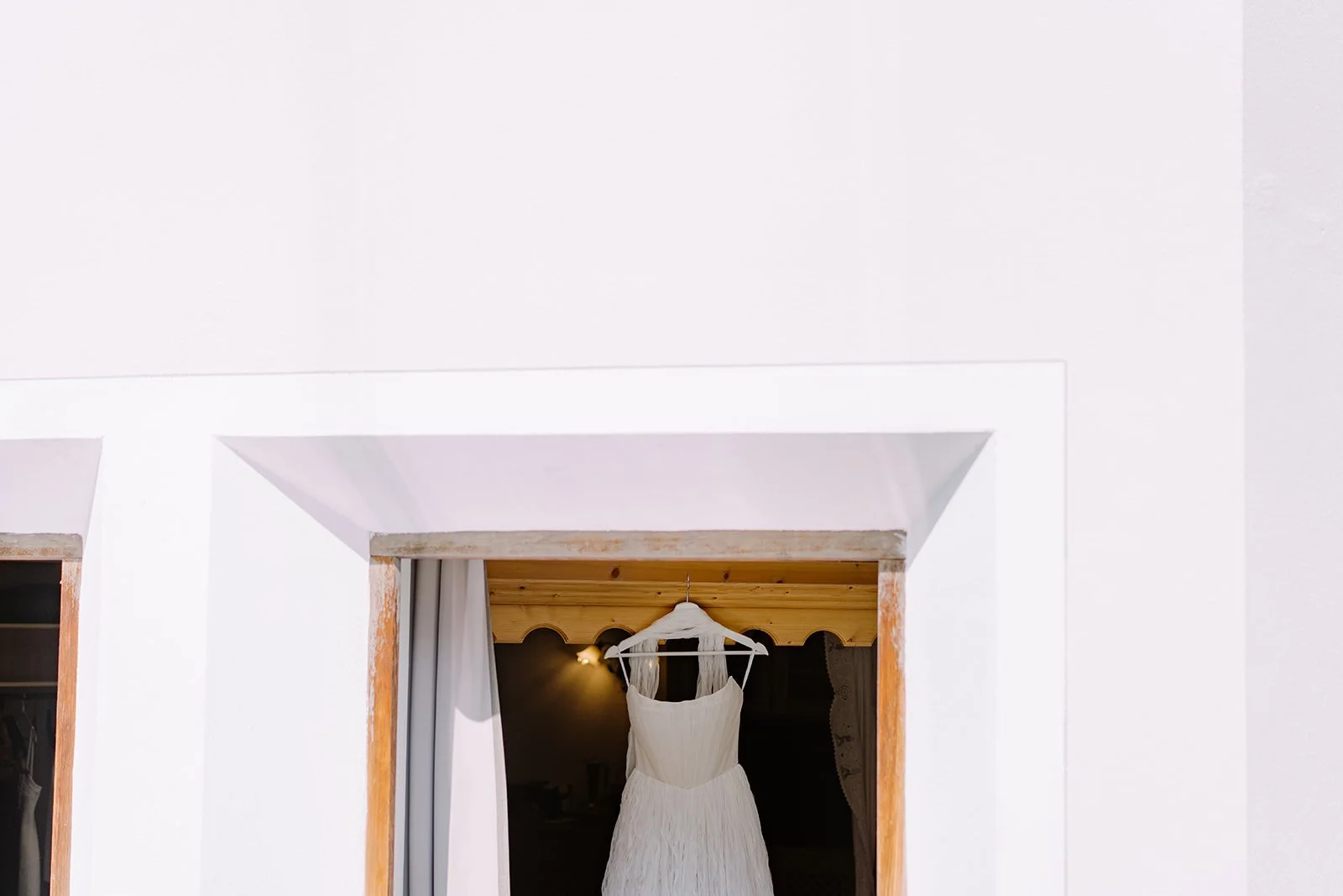 A white wedding dress hanging on a hanger inside a doorway with white walls and a wooden ceiling.