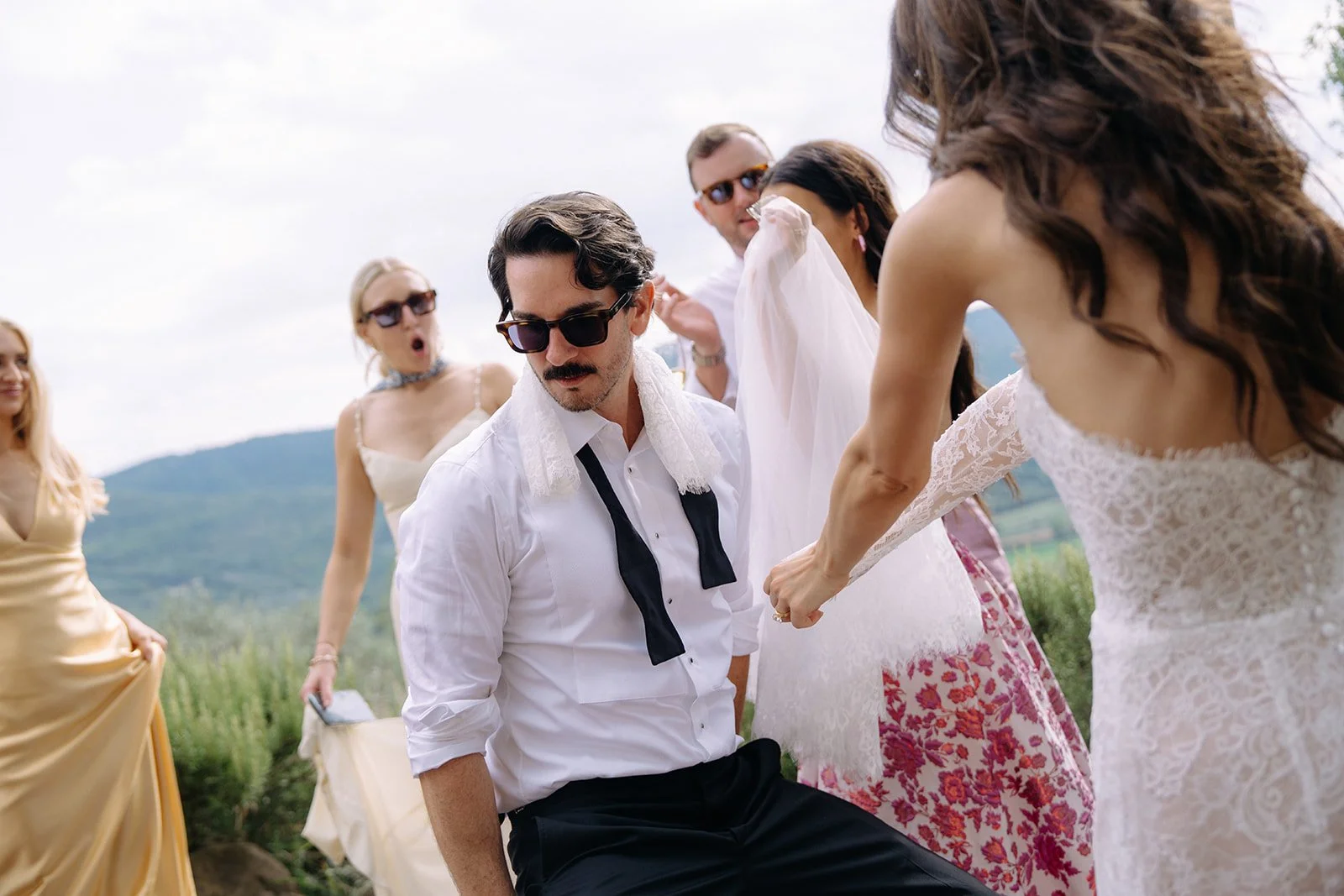 Group of people wearing formal attire outdoors, with mountains in the background.