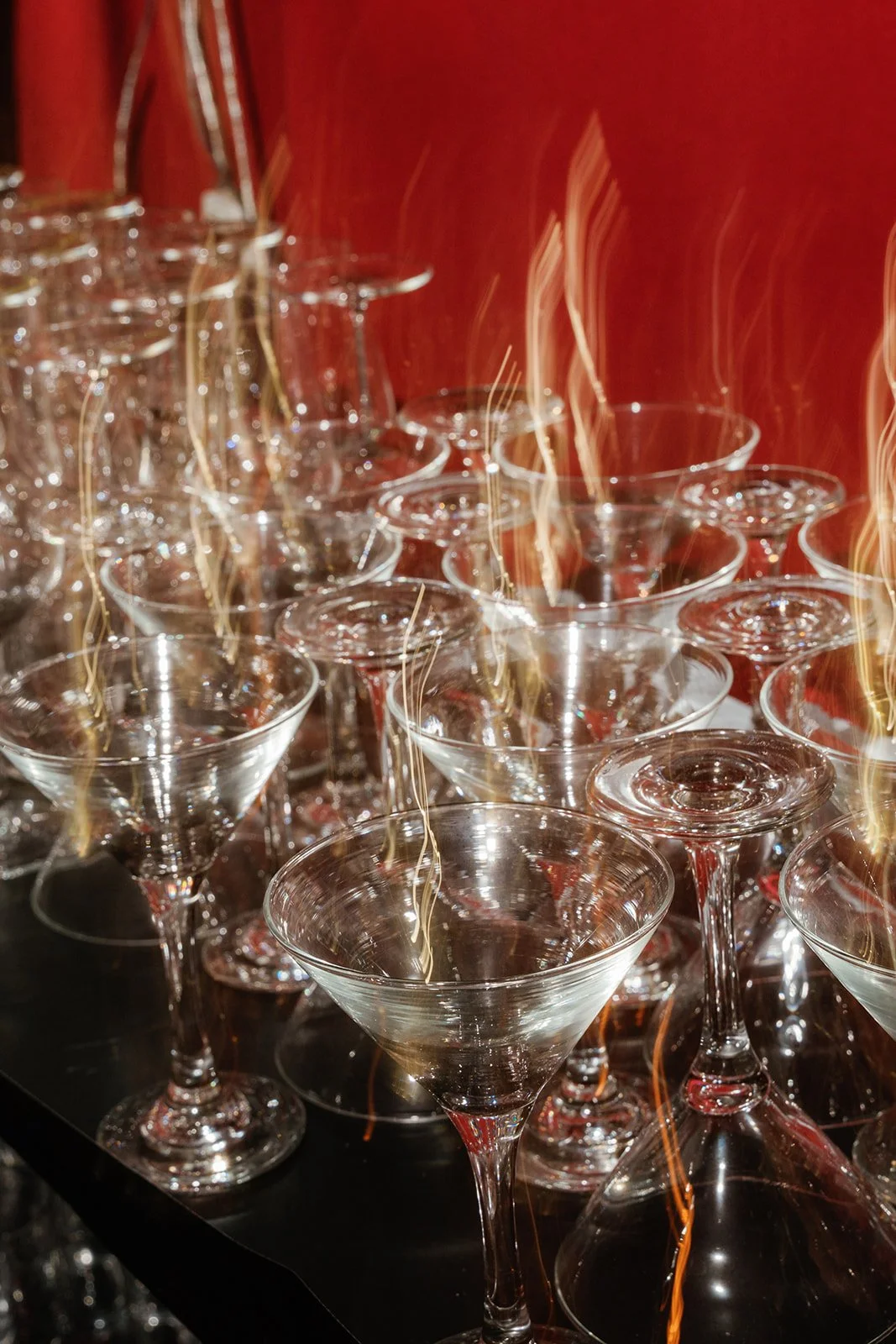 A collection of empty martini glasses arranged on a dark surface with a red background and light reflections.