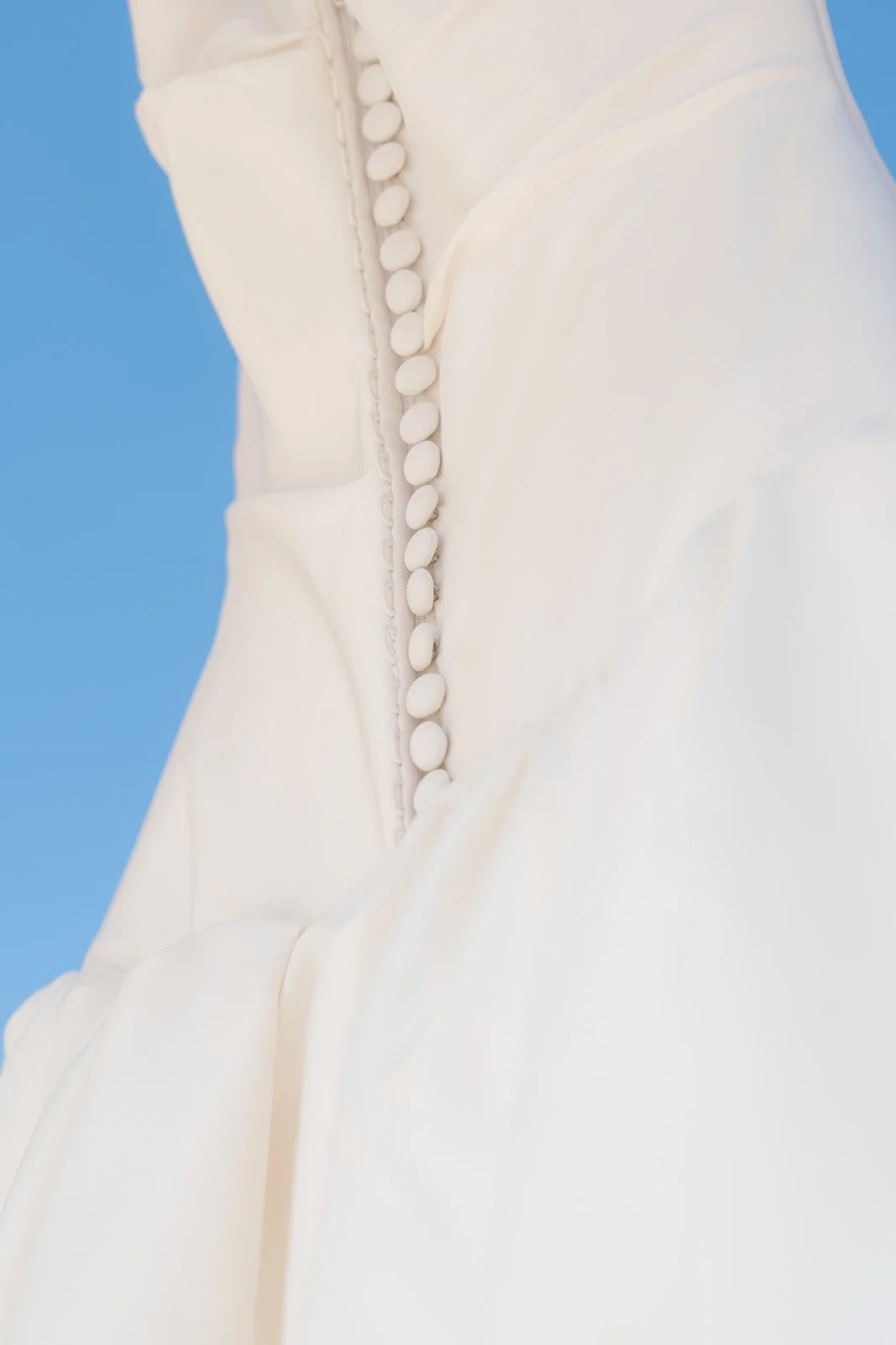 Close-up of a white garment with buttons, possibly a dress or blouse, against a blue background.