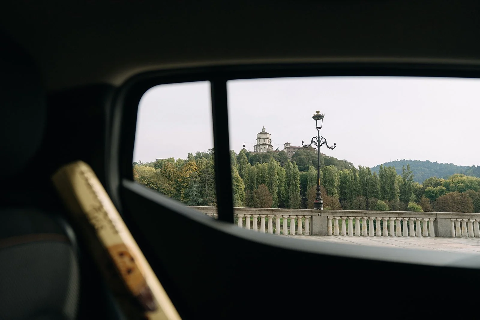 View of a distant hilltop with a building and a streetlamp seen through a car window.