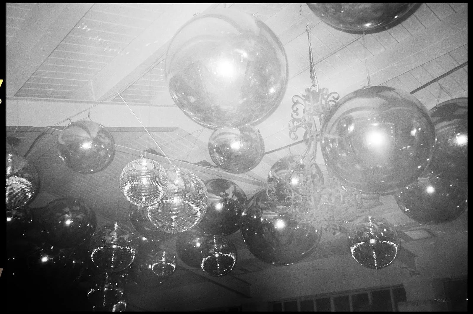 Multiple hanging disco balls of various sizes and a decorative chandelier on a ceiling.