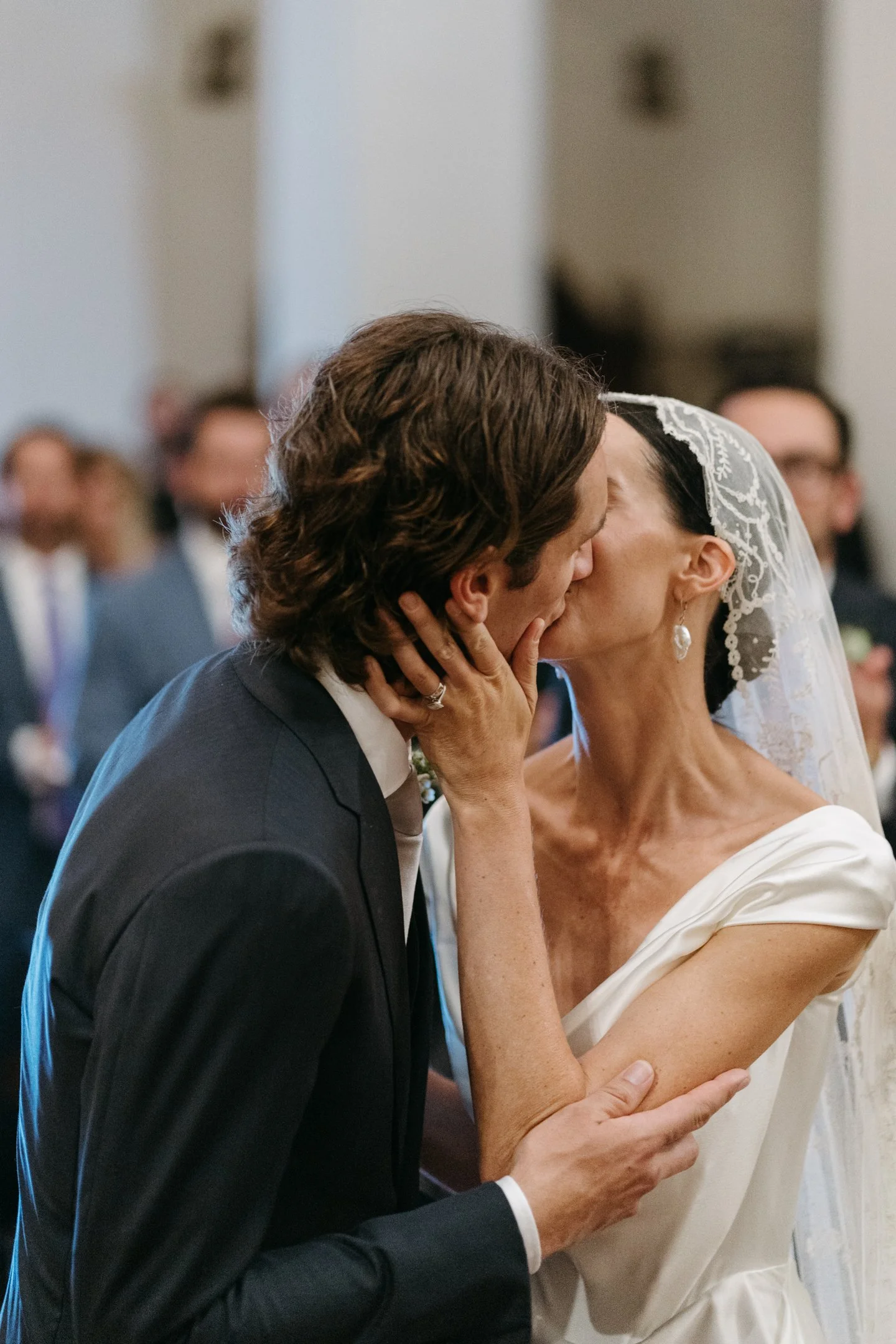 A bride and groom sharing a kiss during their wedding ceremony, with guests in the background.