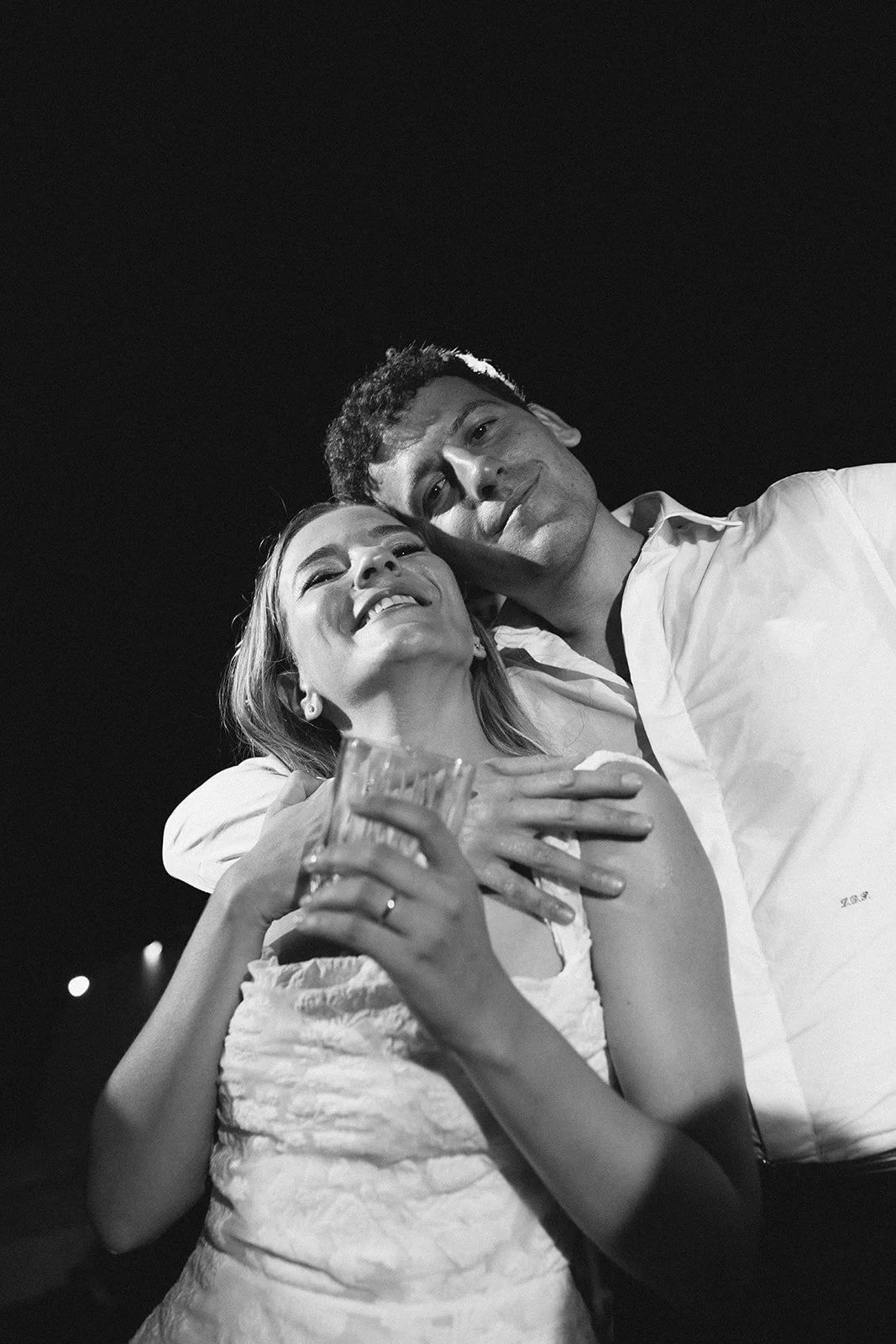 A joyful woman holding a glass, embracing a man, both smiling, in a black and white photo.