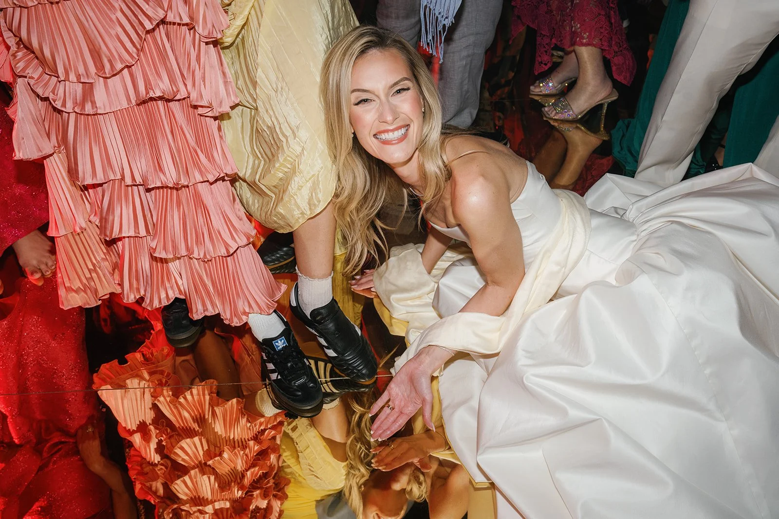 Woman in a white dress kneeling on the floor in a packed, colorful room, smiling at the camera.