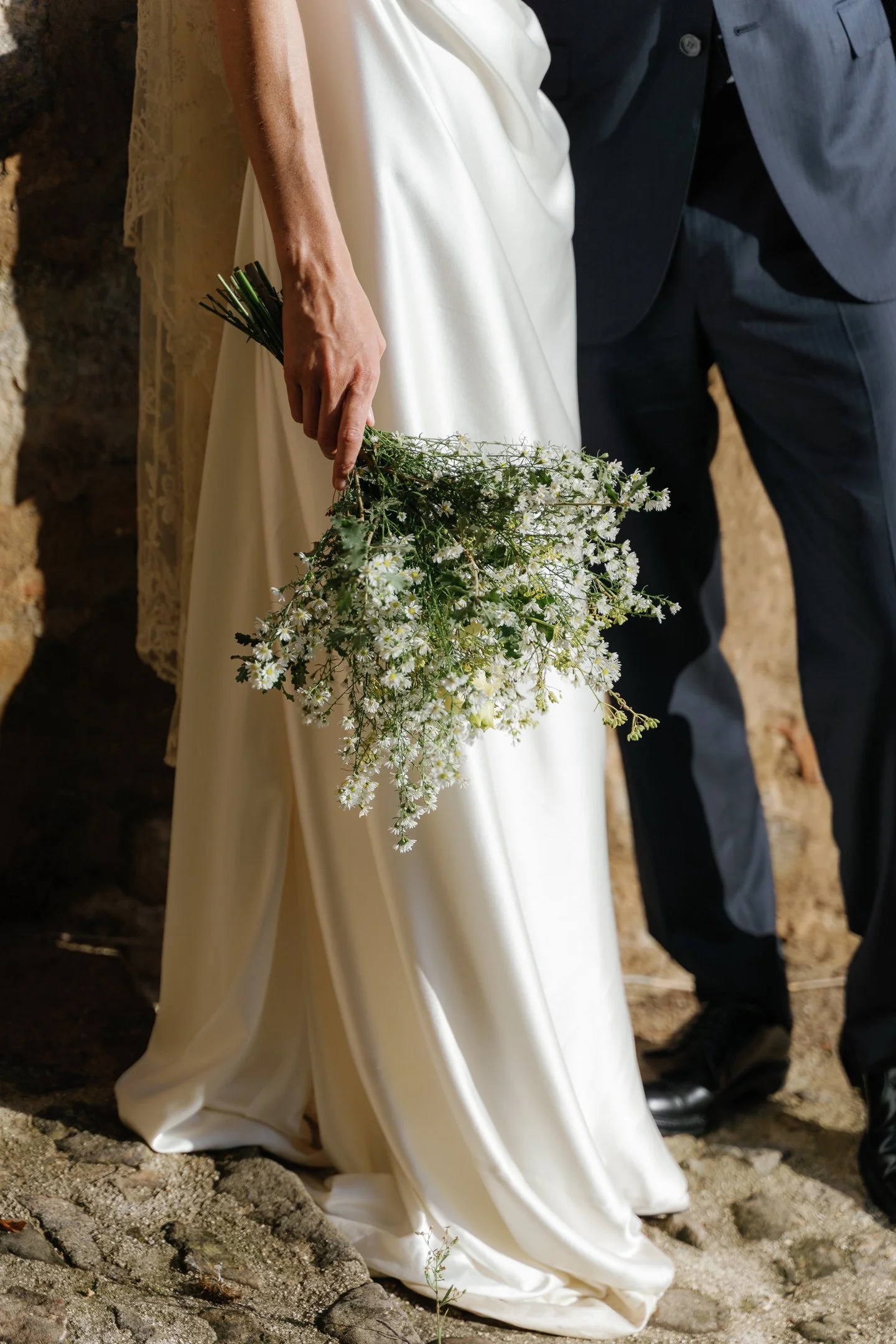 Close-up of a bride holding a bouquet of white flowers at a wedding, with groom standing beside her.