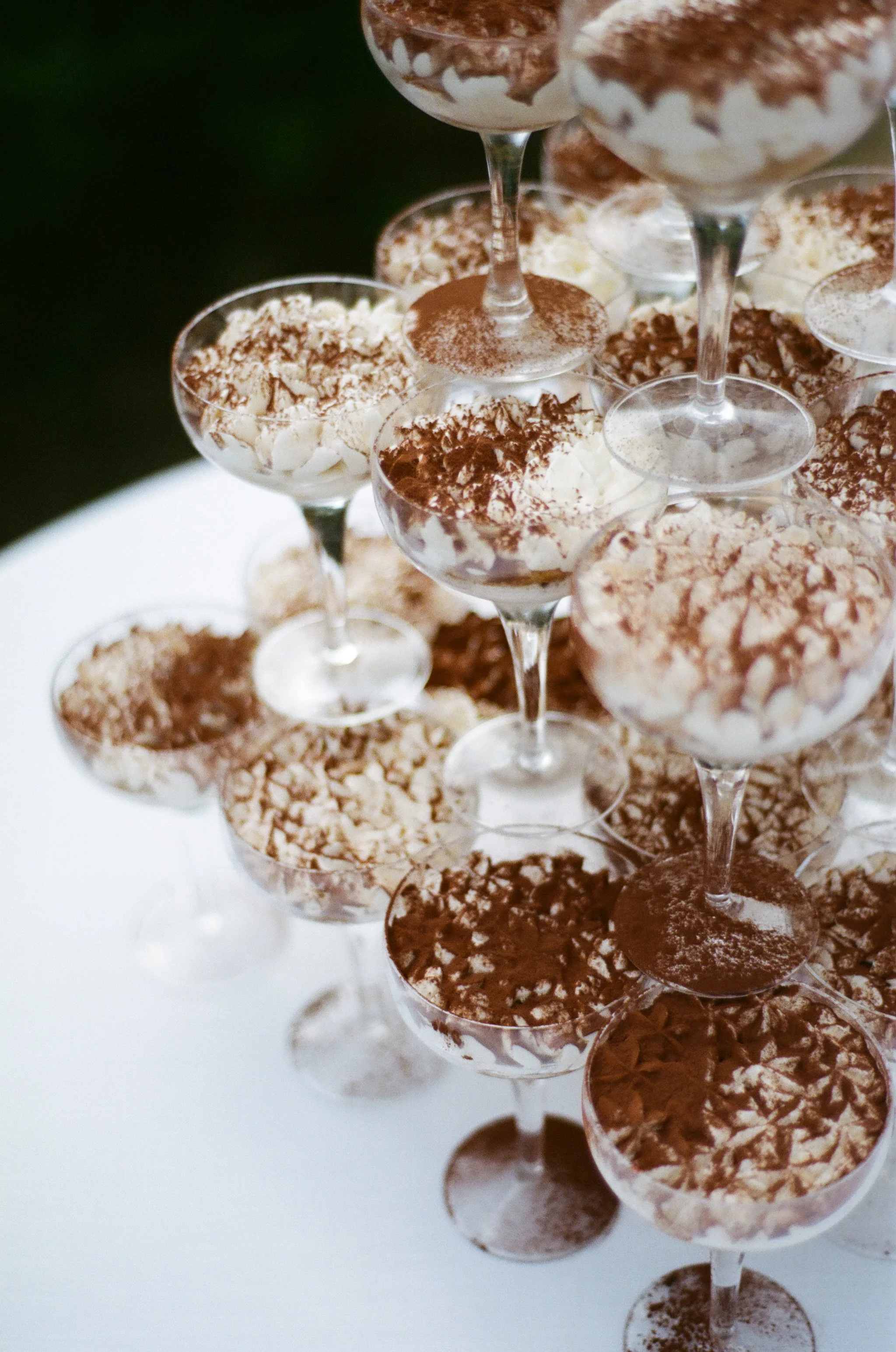 Multiple glass dessert cups filled with tiramisu with layers of cream and cocoa powder, arranged on a white surface.