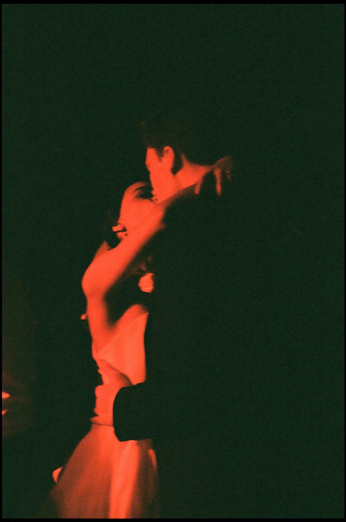 A couple is sharing a dance in a dark, red-lit environment.