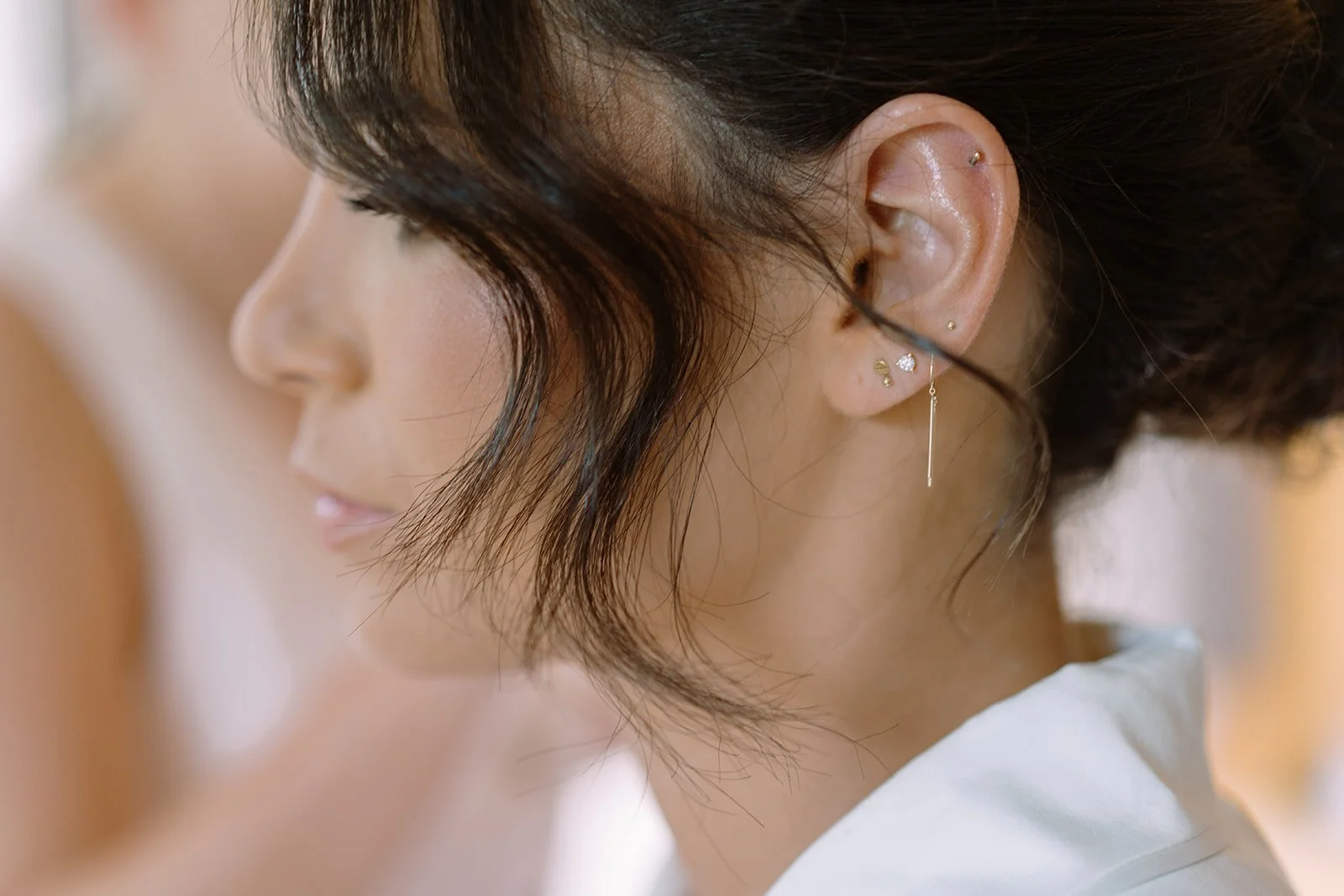 Close-up of a woman with short dark hair, multiple earrings, and a silver dangle earring, with her eyes closed.