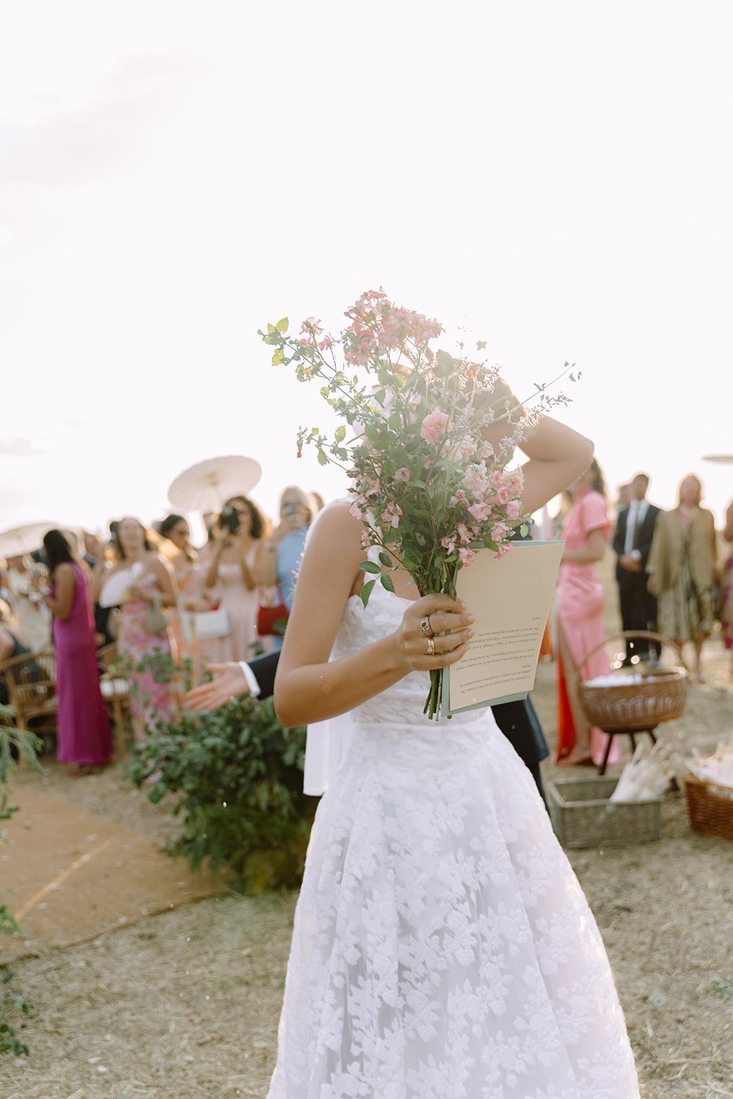 Bride holding a bouquet of pink flowers at an outdoor wedding reception.