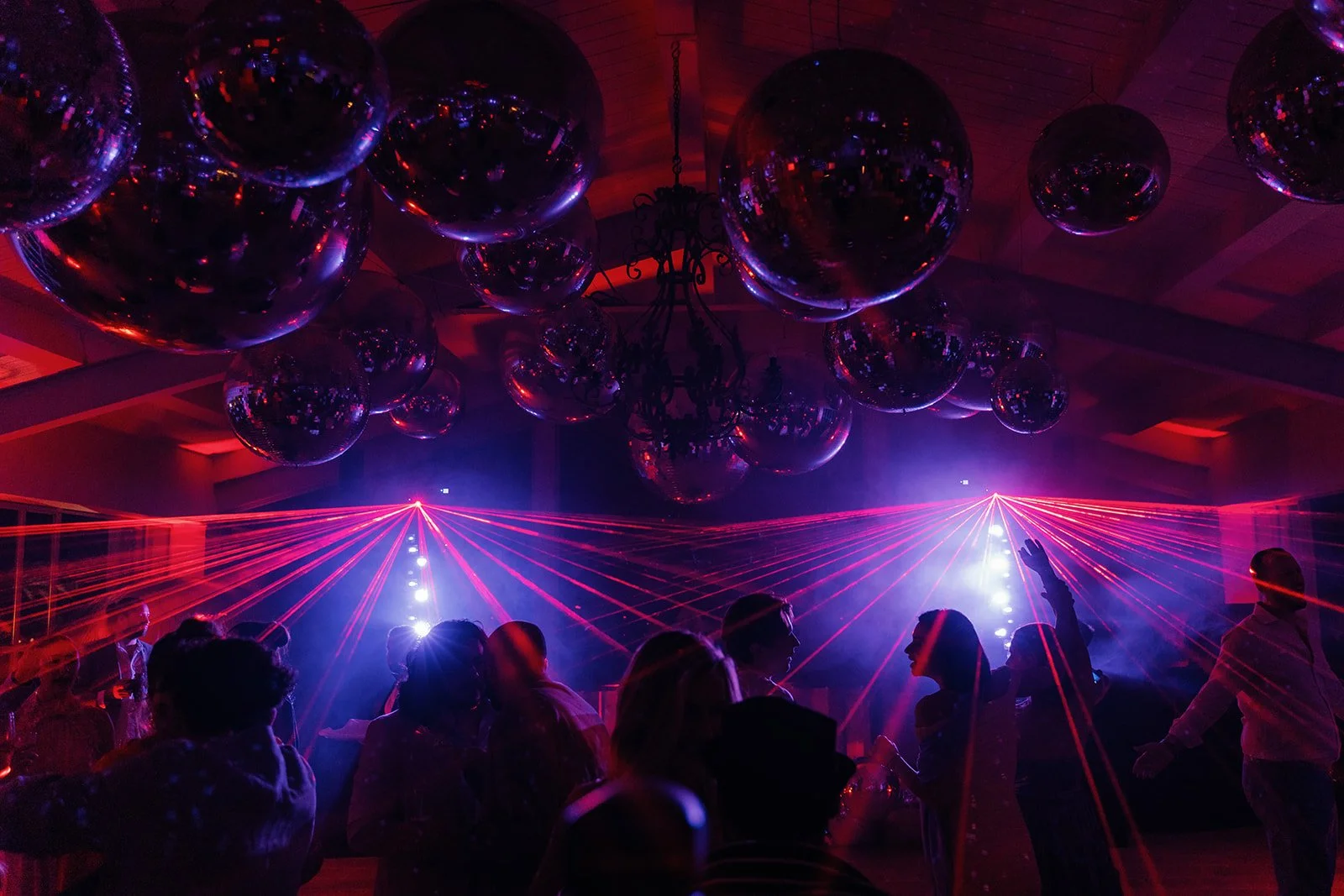 People dancing at a party or nightclub with laser lights, reflective disco balls on the ceiling, and colorful lighting.