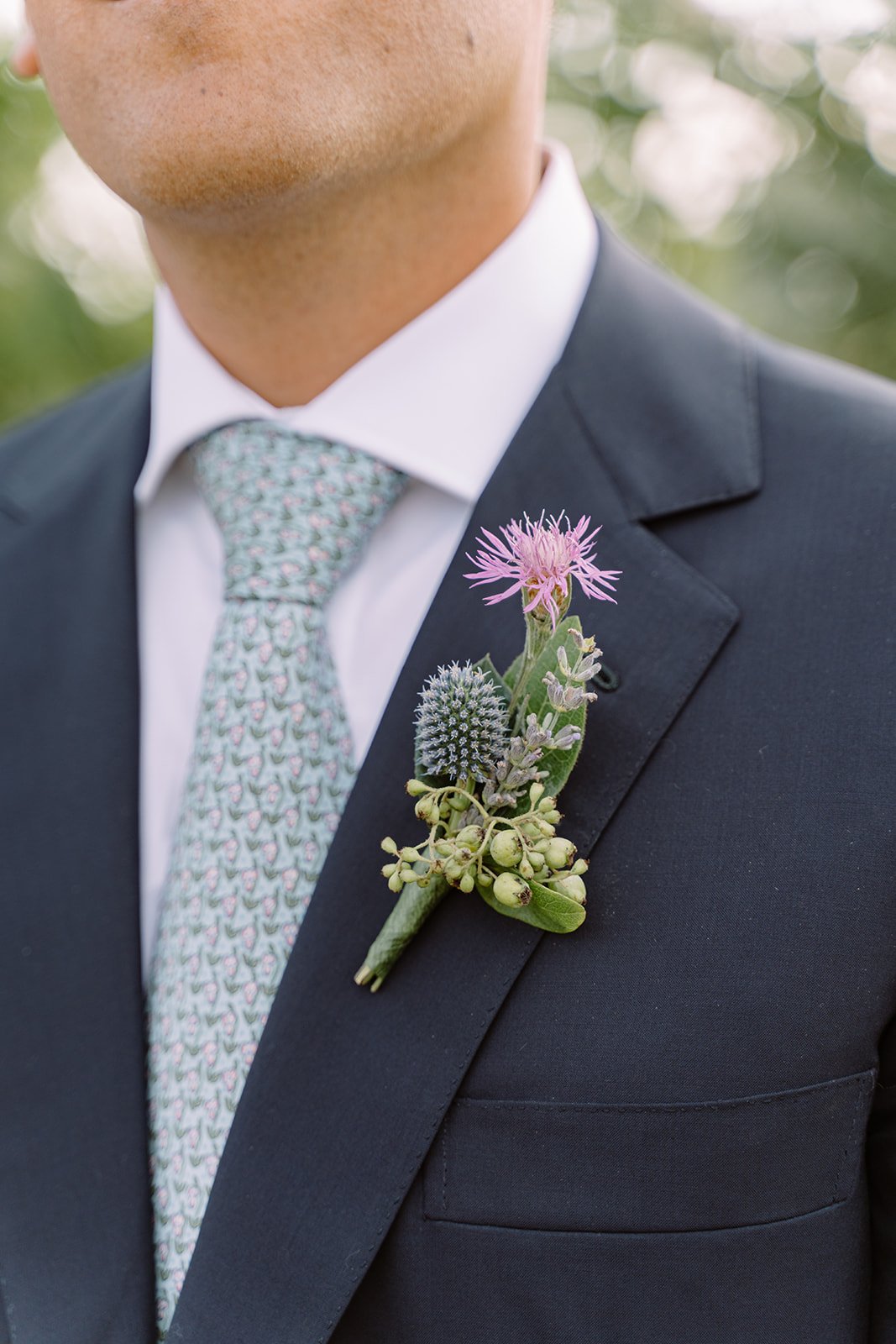 Close-up of a man's suit with a pink and purple flower boutonniere attached to the lapel.
