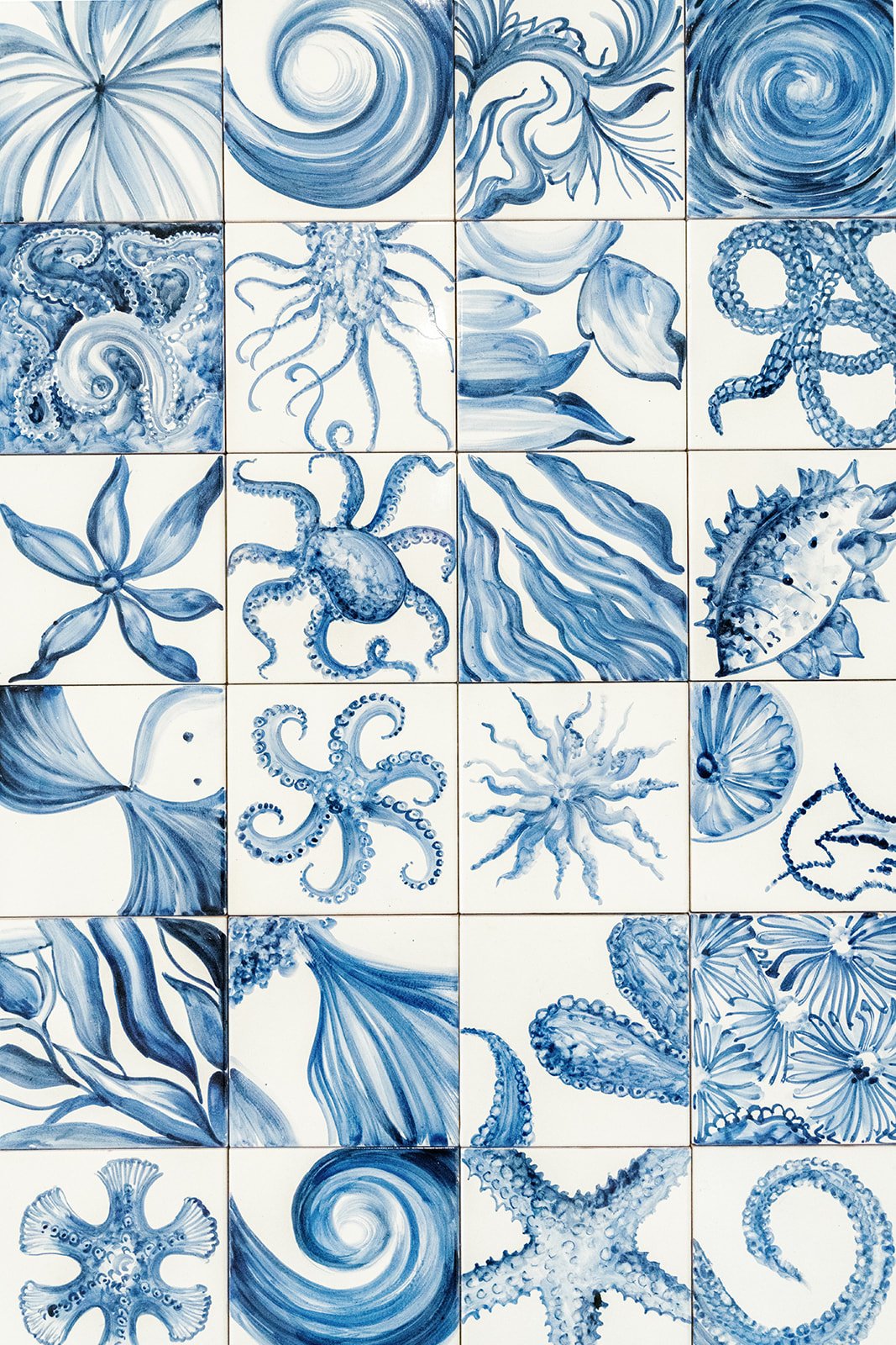 A mosaic of 20 ceramic tiles, each featuring a blue and white painting of an ocean creature or seaweed, including octopuses, jellyfish, starfish, shells, and other marine life.