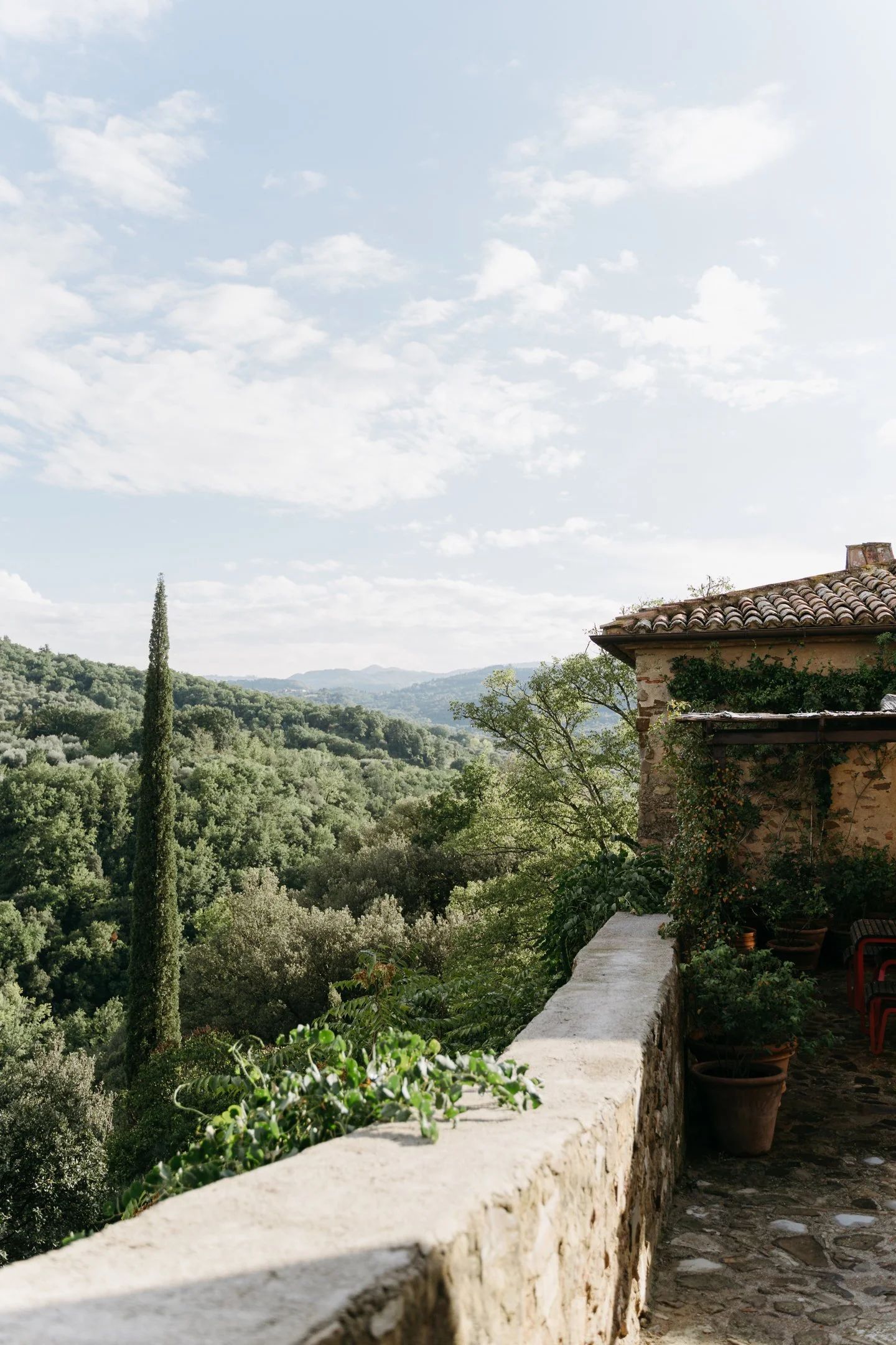 View from a rustic balcony overlooking a lush, green, hilly landscape with scattered trees, under a partly cloudy sky.