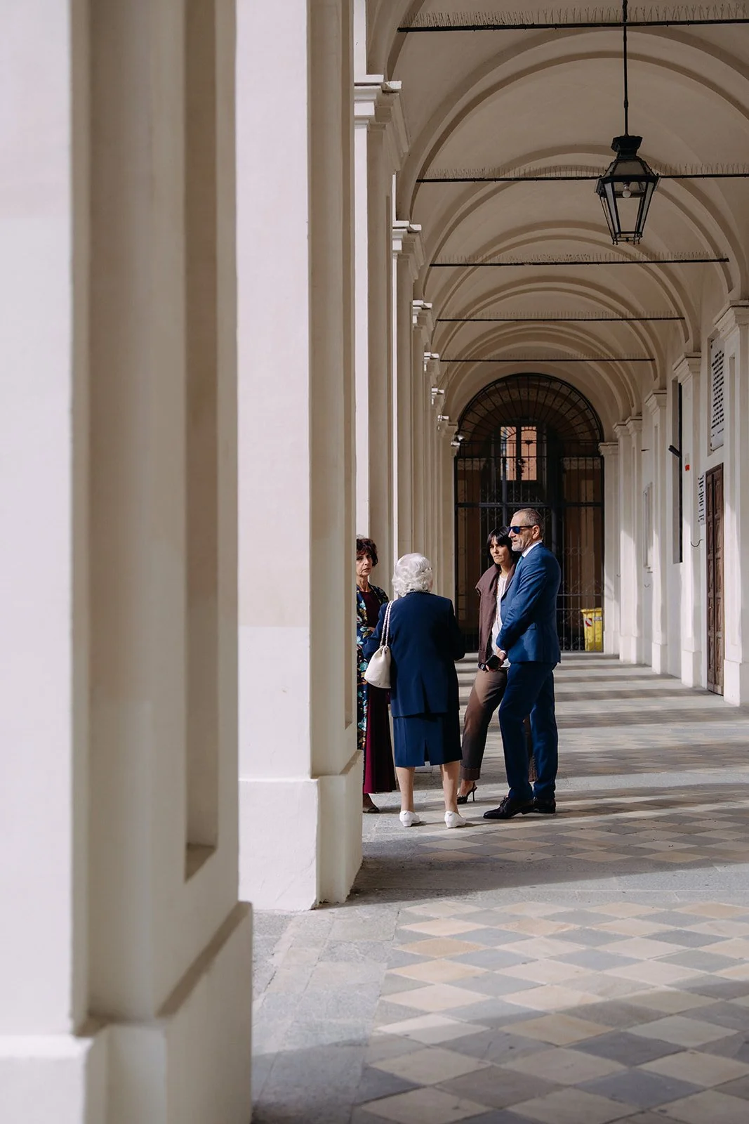 Four people standing and talking in a covered corridor with vaulted ceilings and hanging lanterns.