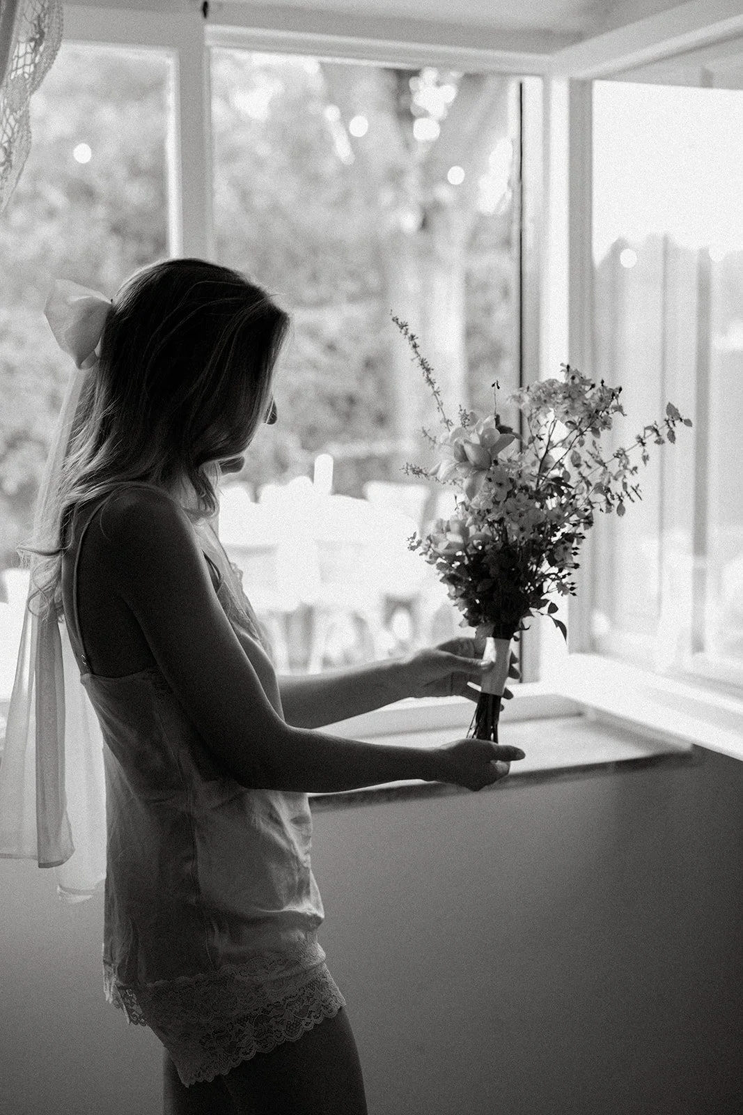 Silhouette of a woman holding a bouquet of flowers next to a window.