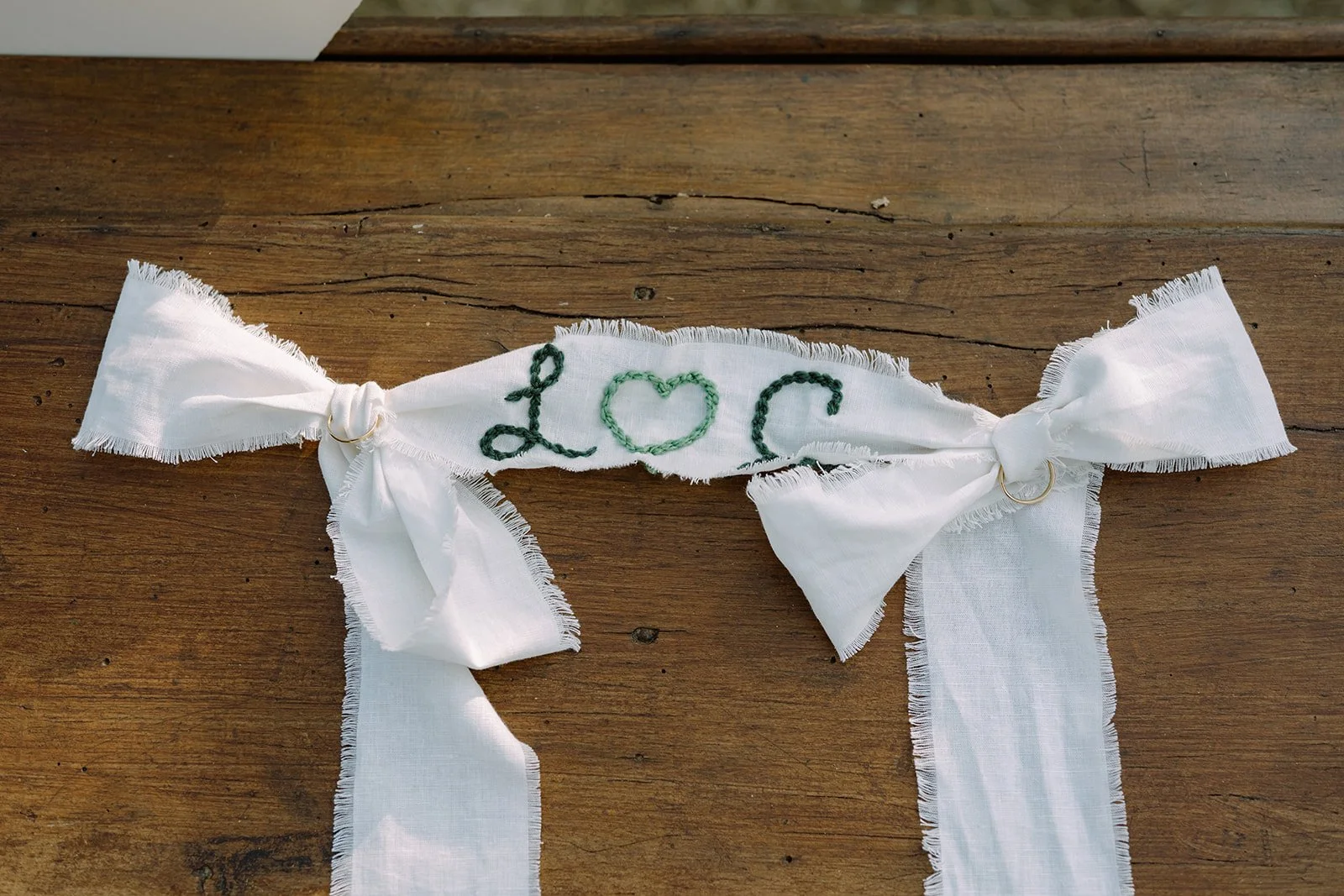 White fabric ribbon with embroidered green text 'LOVE' and two loops, tied into bows on a wooden surface.