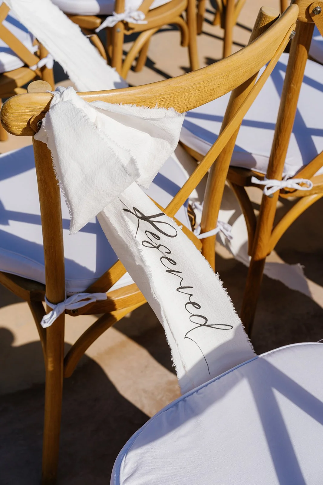 Close-up of a wooden chair decorated with a white fabric ribbon with the word 'reserved' written on it, tied to the chair's backrest in an outdoor setting.
