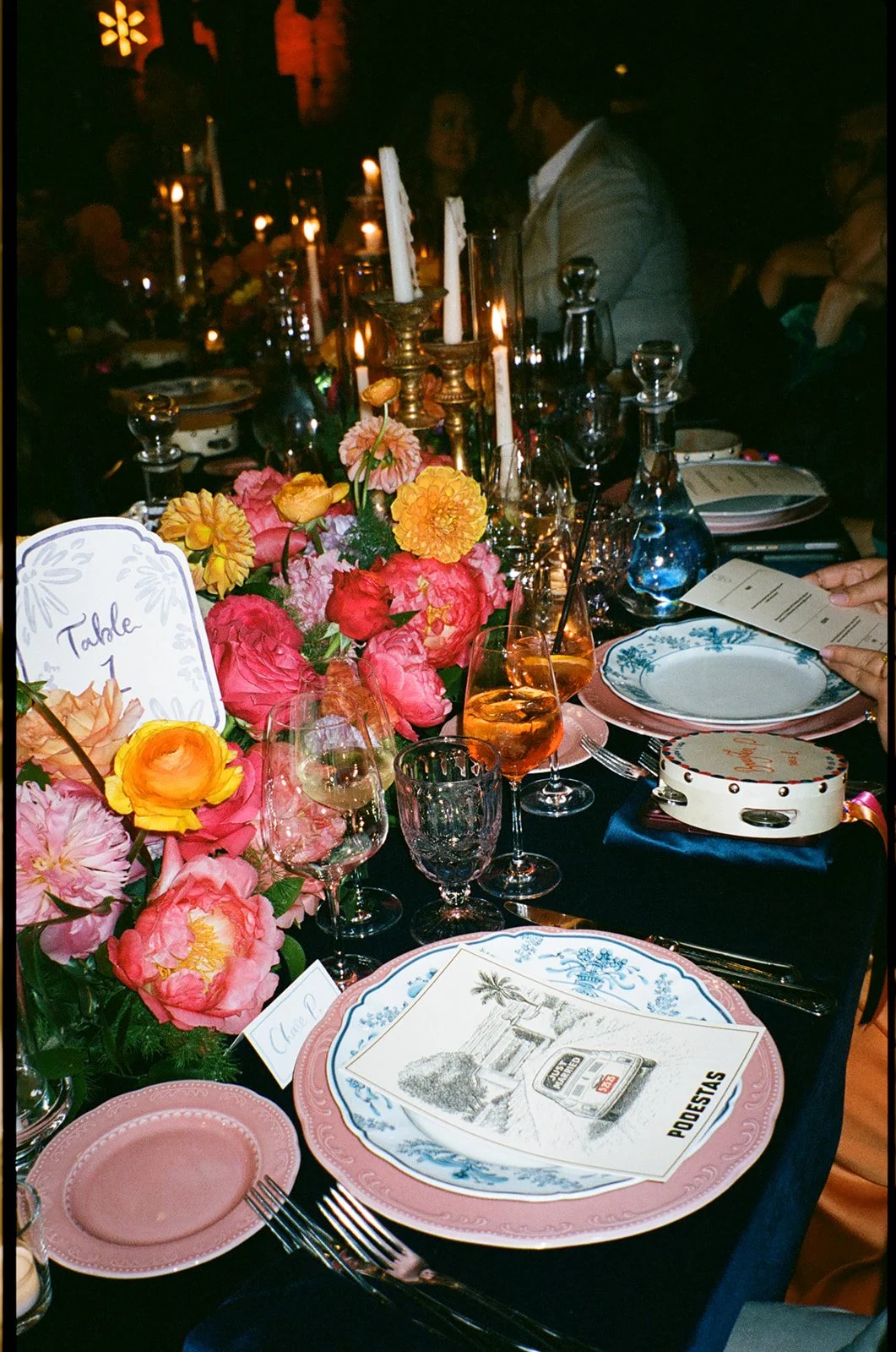 A decorated banquet table with a floral centerpiece, candles, wine glasses, plates, and a menu, set for a formal event.